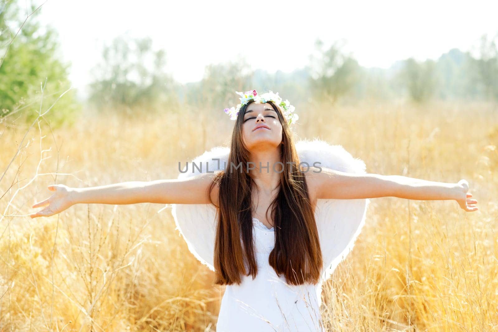 Angel etchnic woman in golden field with feather white wings and flowers crown