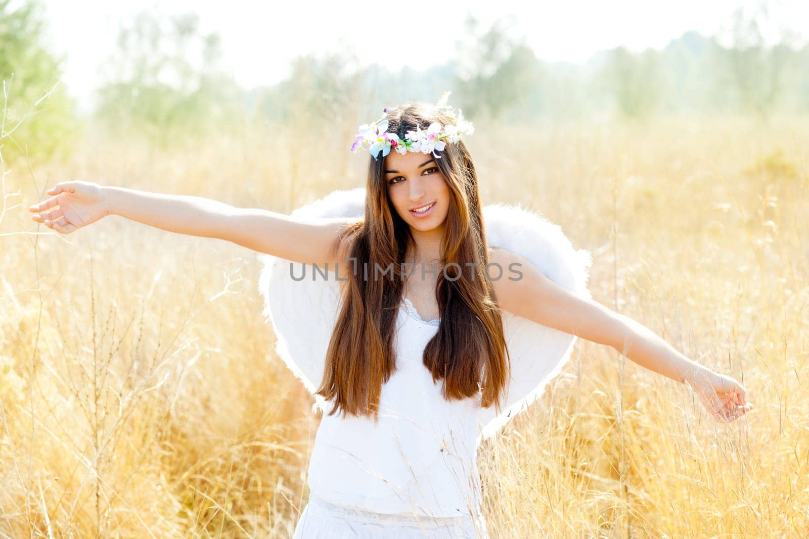 Angel etchnic woman in golden field with feather white wings and flowers crown