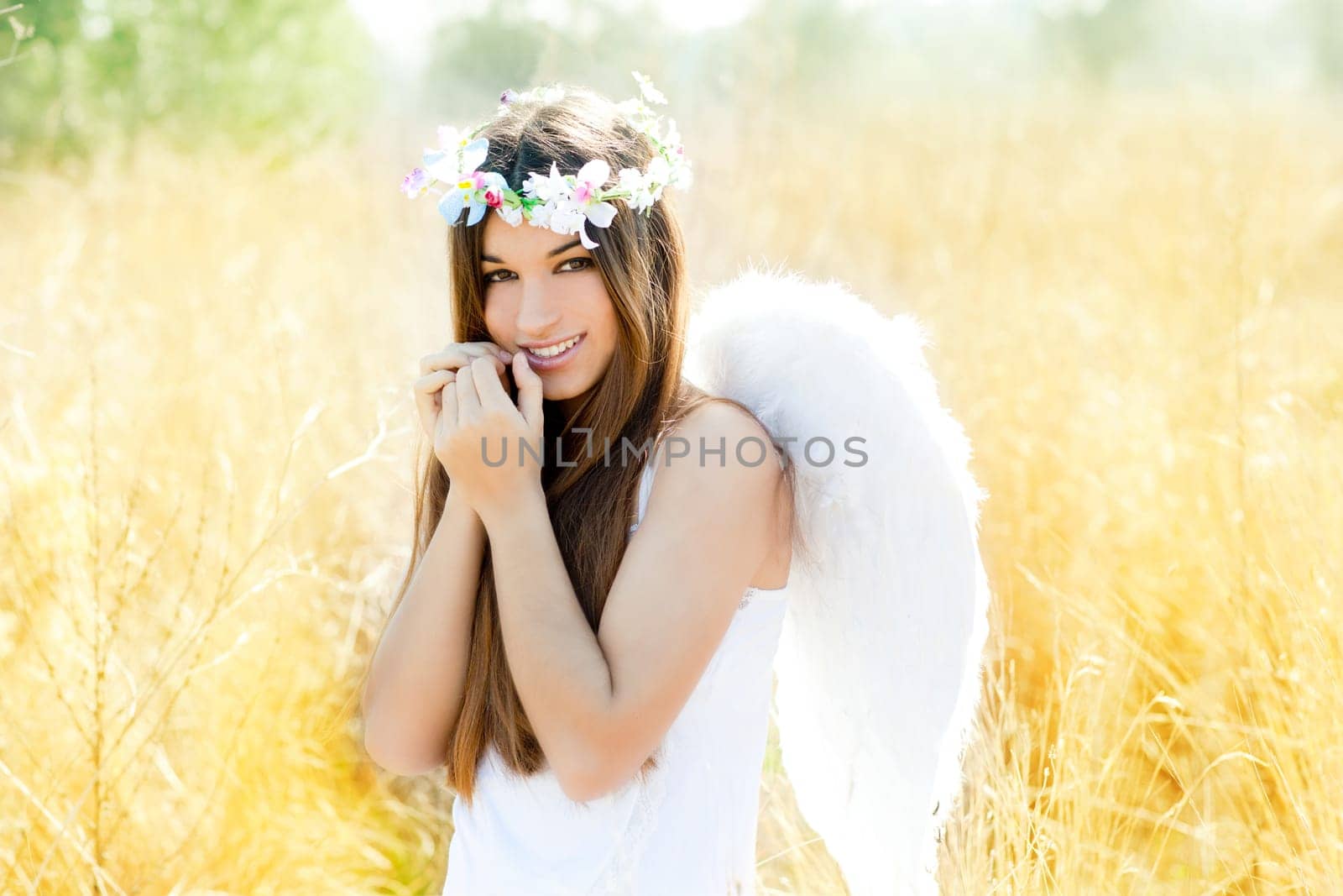 Angel etchnic woman in golden field with feather white wings and flowers crown