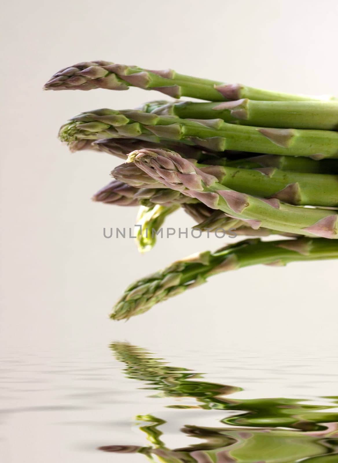 A bunch of asparagus reflected in water on a gray background