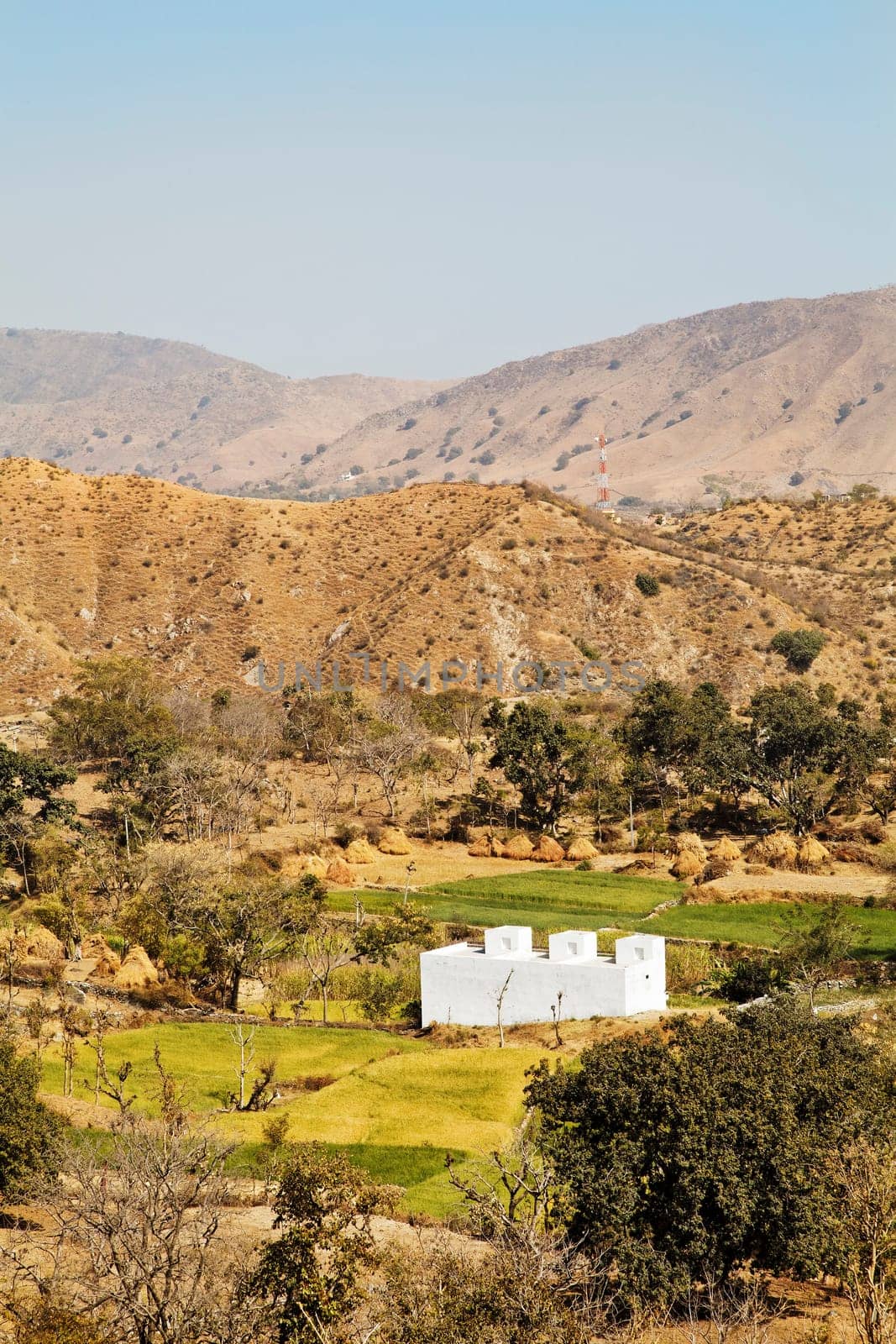 Vertical of farmland patterns of rural Rajasthan near Kumbhalgarth India with whit farm house, distant hills and blue sky