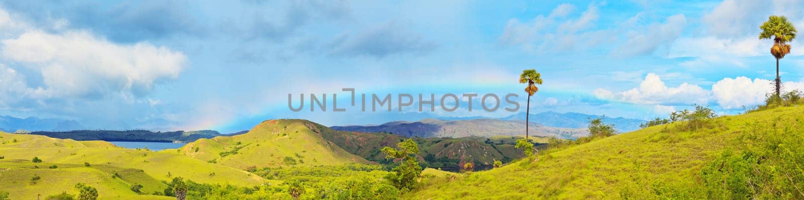 Panorama of the Rinca island. Rainbow over savanna