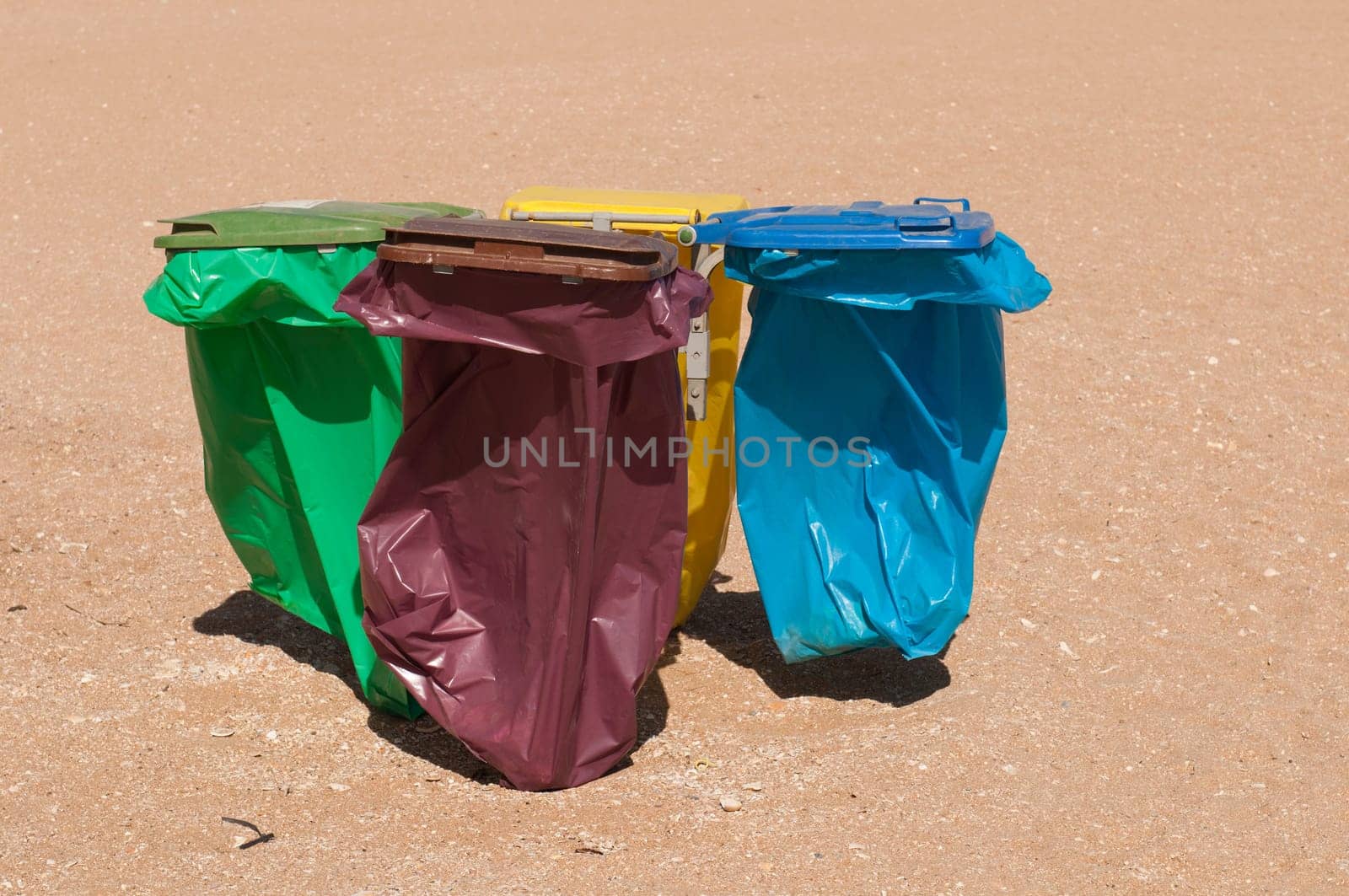 four colorful recycle bins on a beach