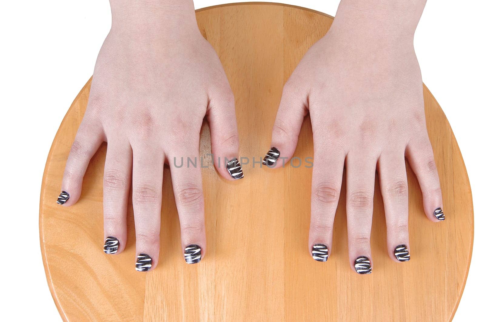 The hands of a young teenage girl with nice polished finger nails,  resting on a round wood chair.
