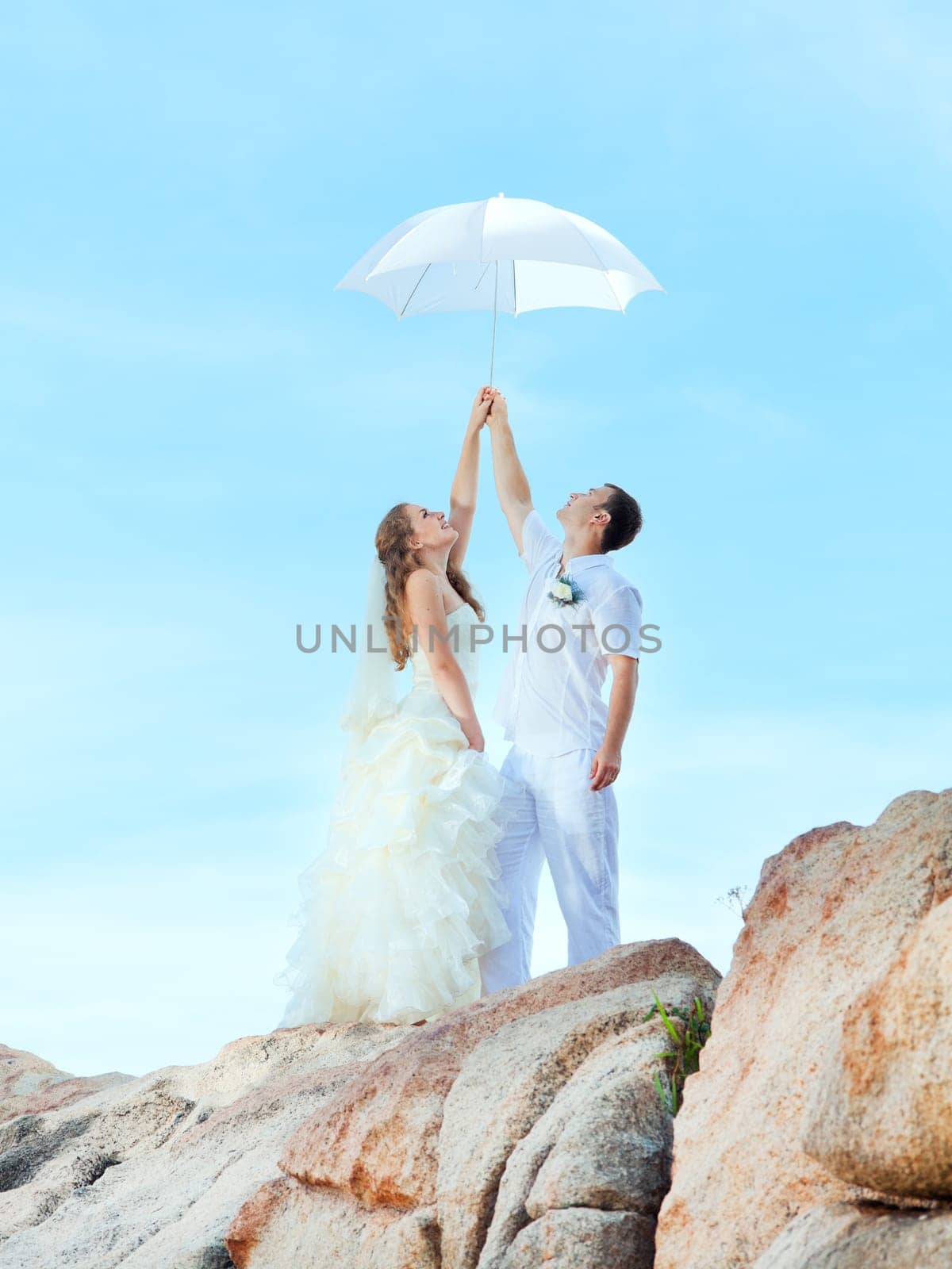 Bride and groom holding an umbrella on a rock.