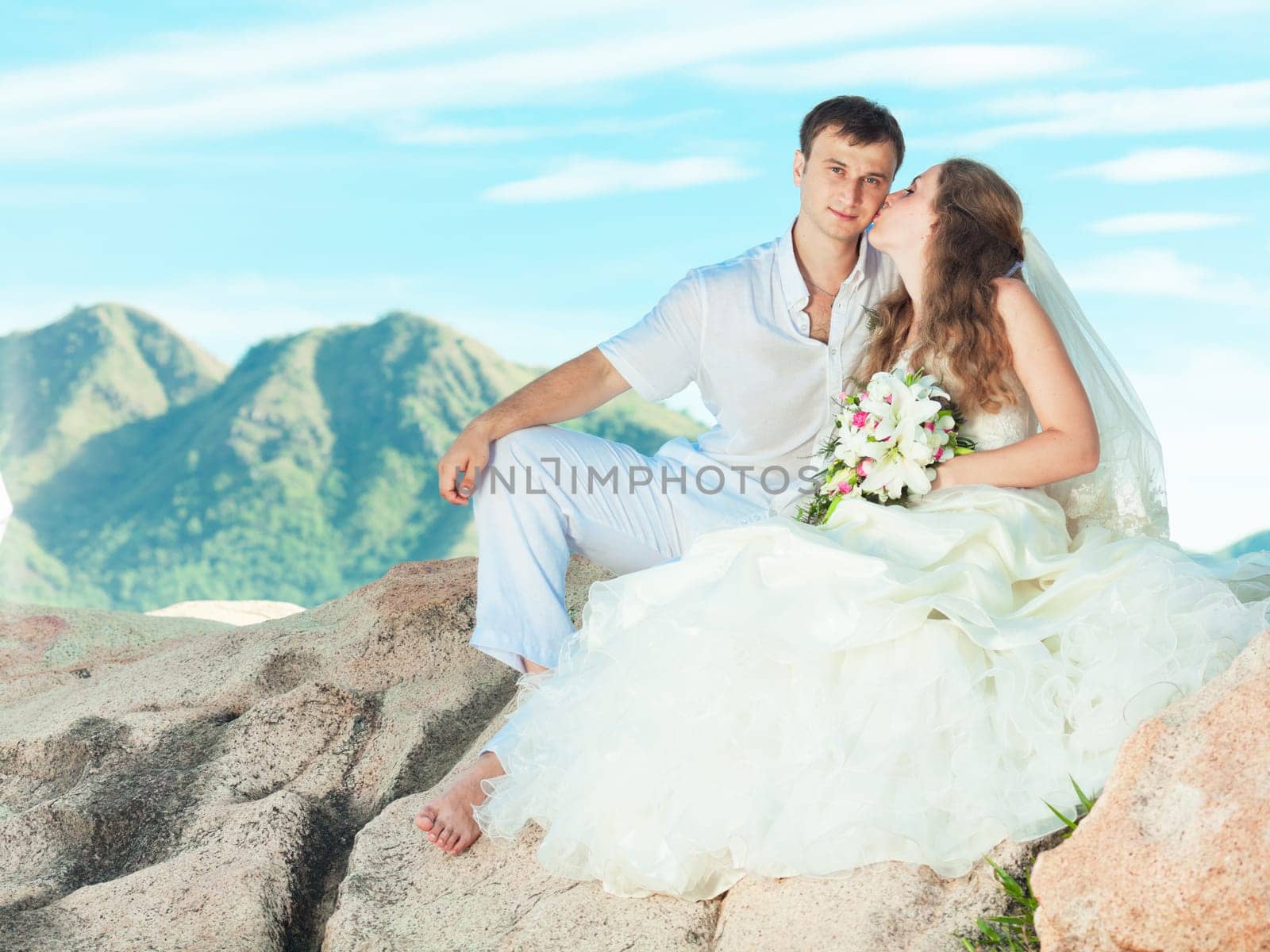 Bride kissing groom on the rock. Mountain on background