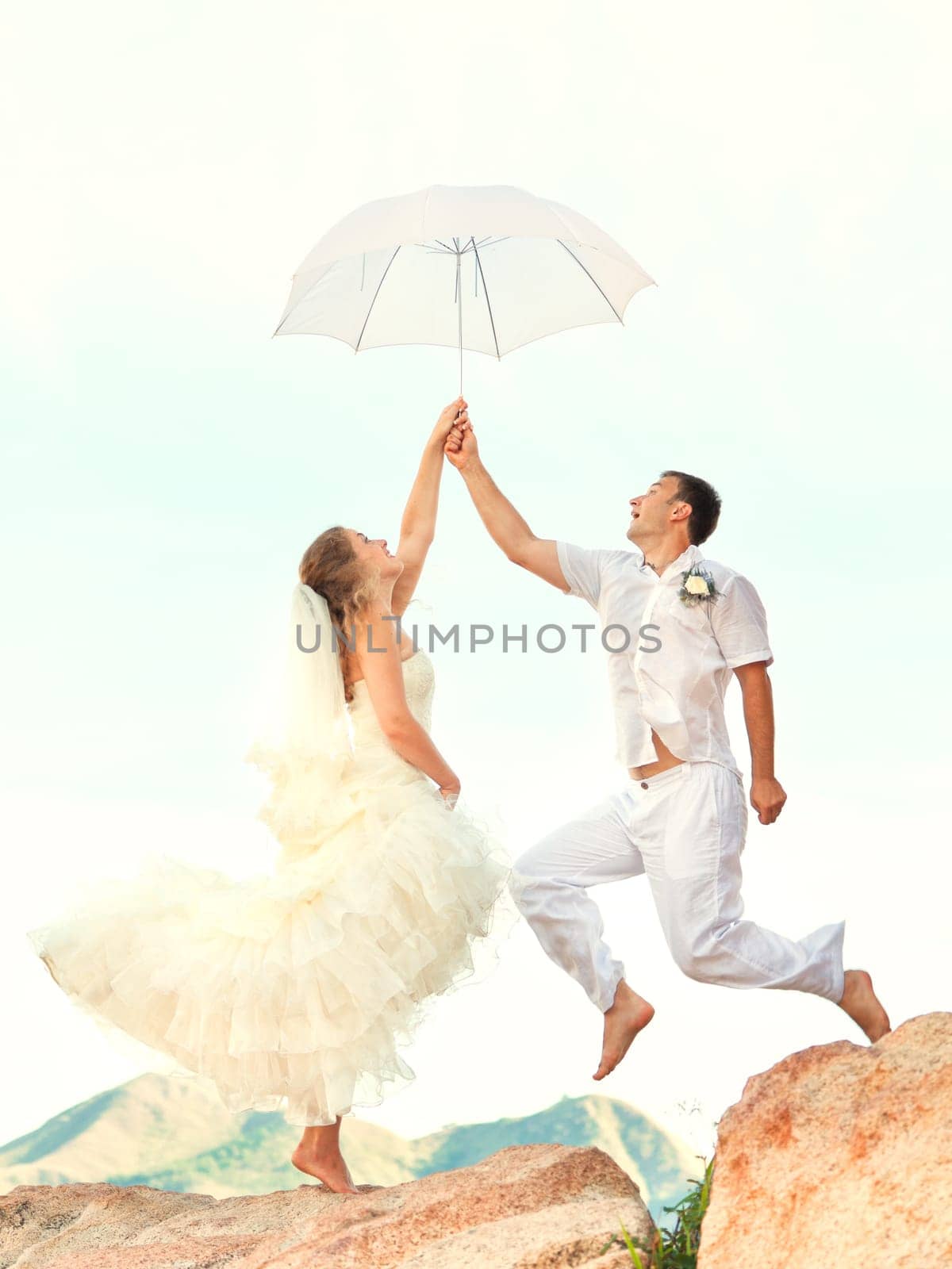 Bride and groom jumping on a rock with umbrella
