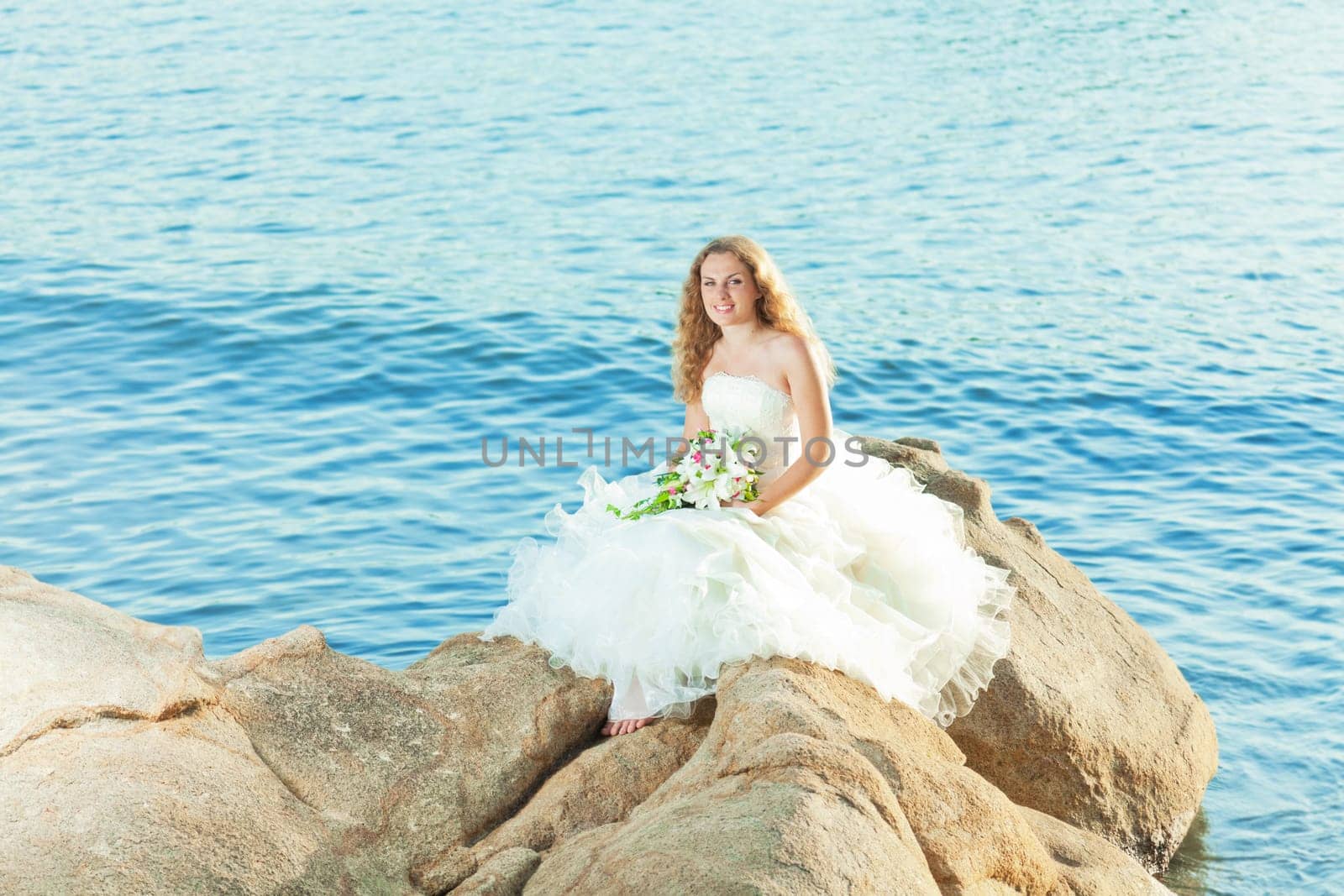 Beautiful bride sitting on a rock in a sea