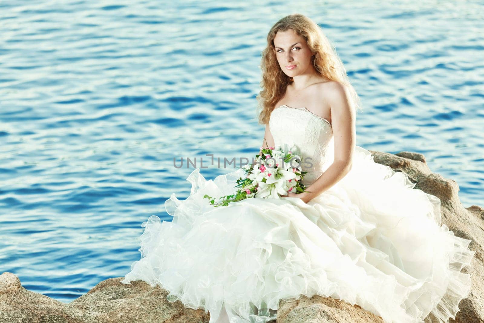 Beautiful bride sitting on a rock in a sea
