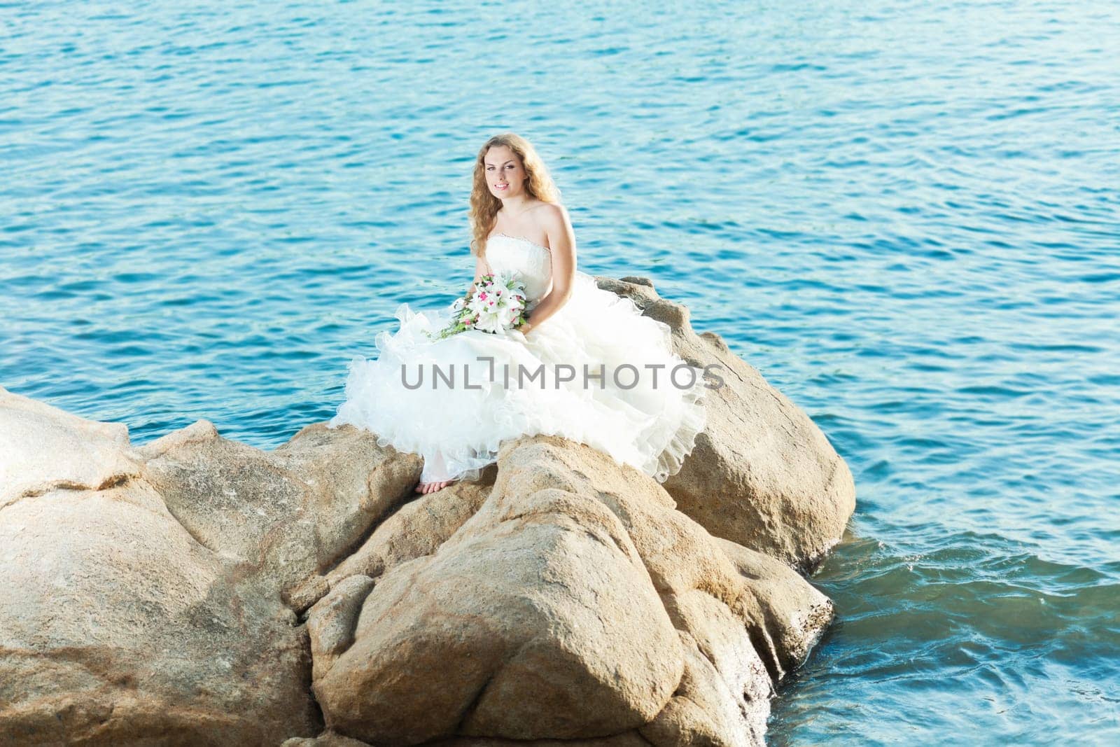 Beautiful bride sitting on a rock in a sea