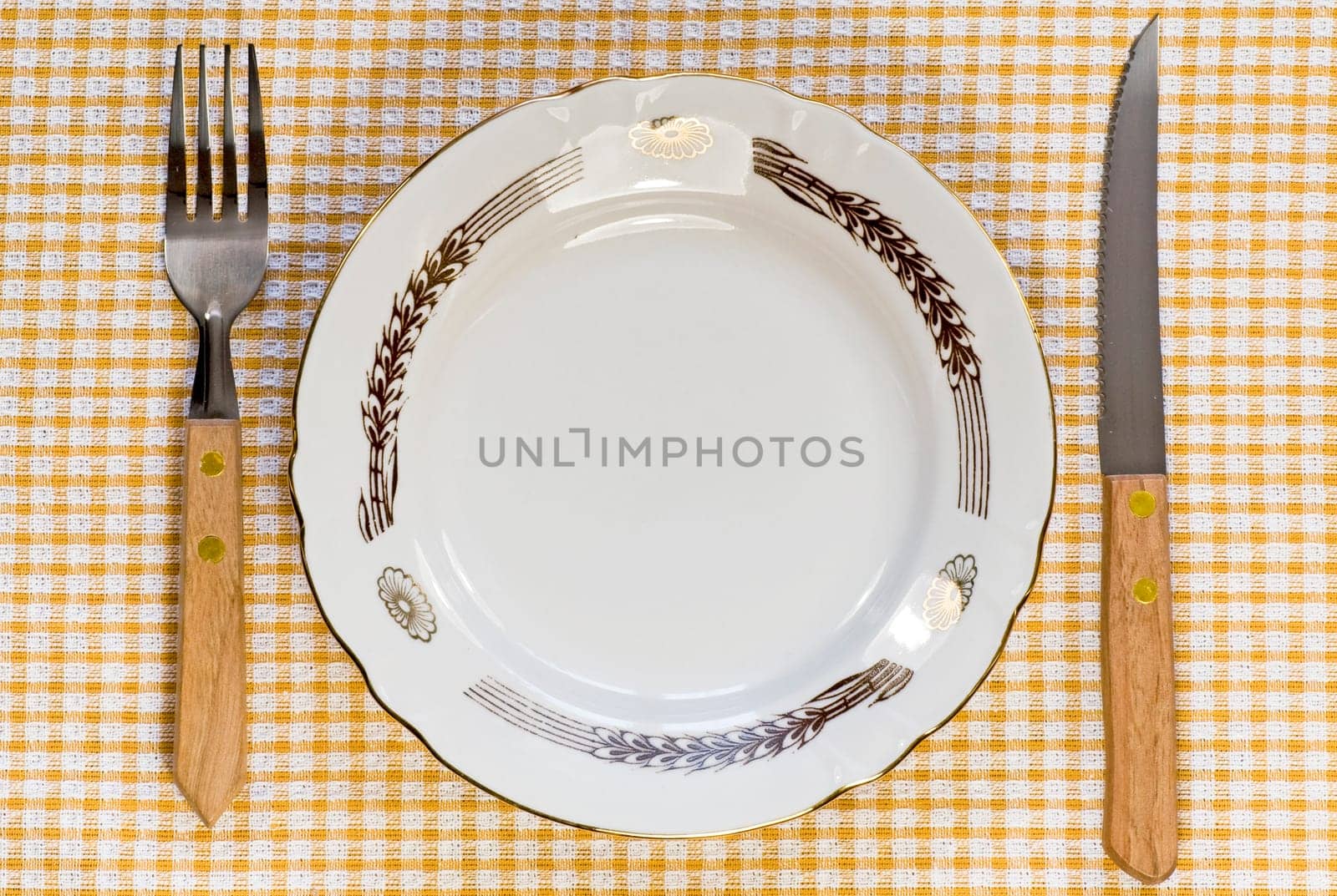 Empty dinner plate with fork and knife on tablecloth