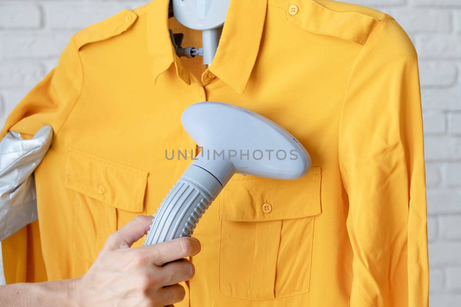 female hand using vertical steamer steaming yellow shirt. steam for ironing clothes. household appliances for the home.
