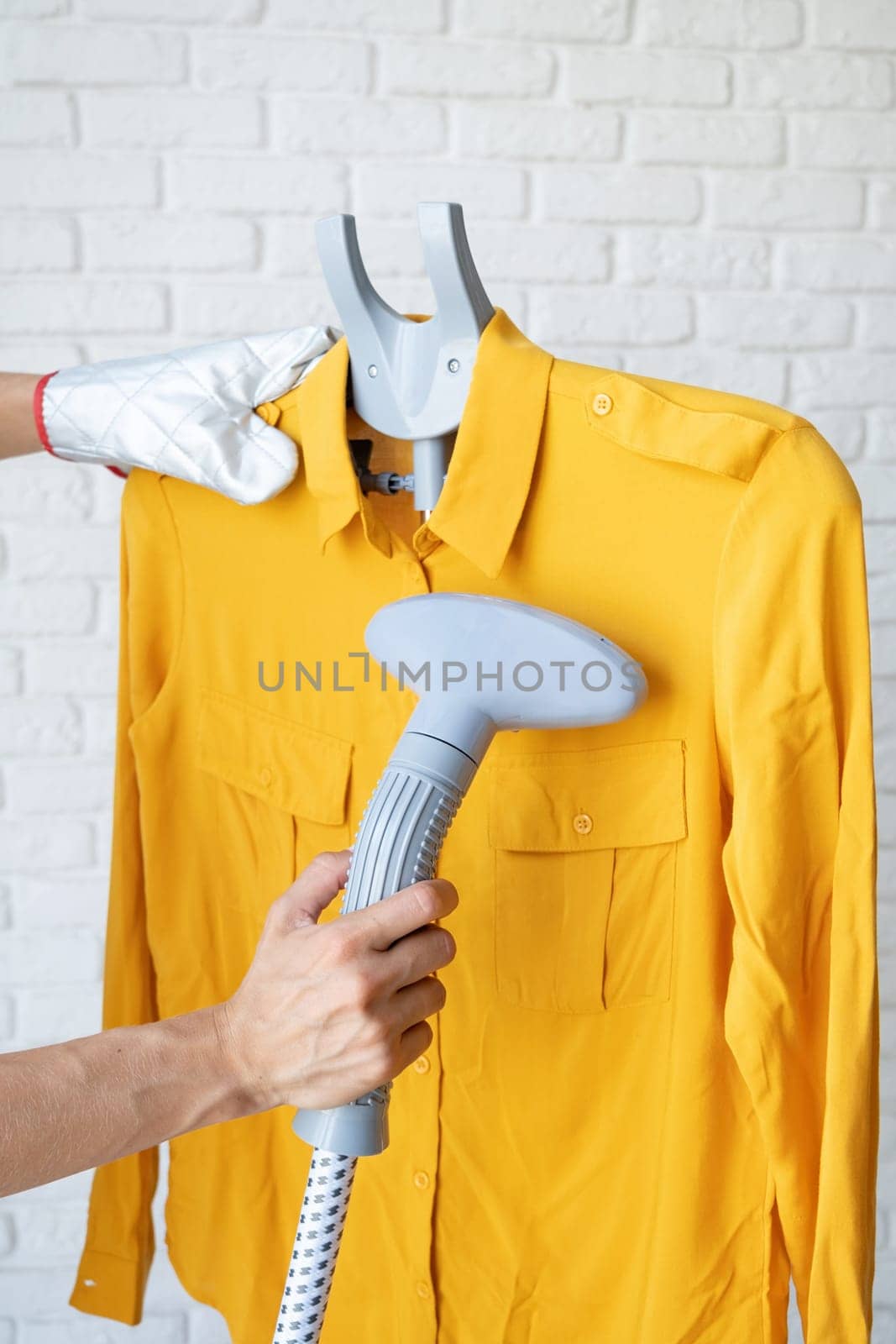 female hand using vertical steamer steaming yellow shirt. steam for ironing clothes. household appliances for the home.