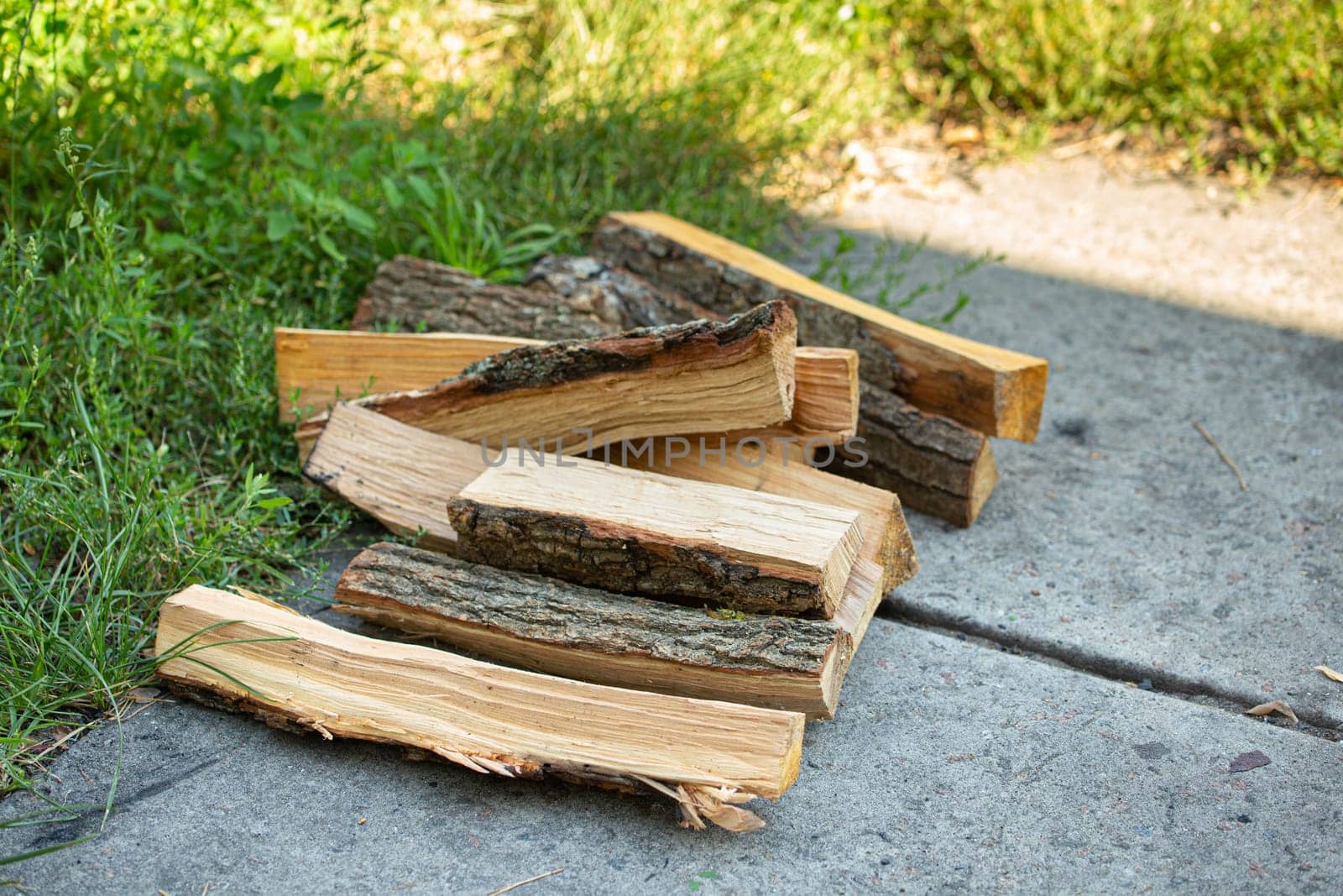 Wood pieces for firewood piled on green backyard in summer waiting to be used for grill or barbecue on picnic..
