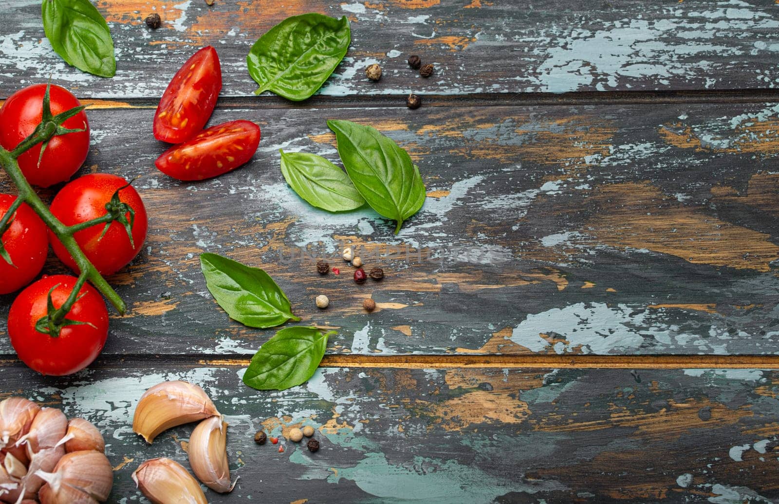 Food cooking border with cherry tomatoes, fresh green basil and garlic cloves top view on rustic colourful wooden background, ingredients for preparing meal, copy space.