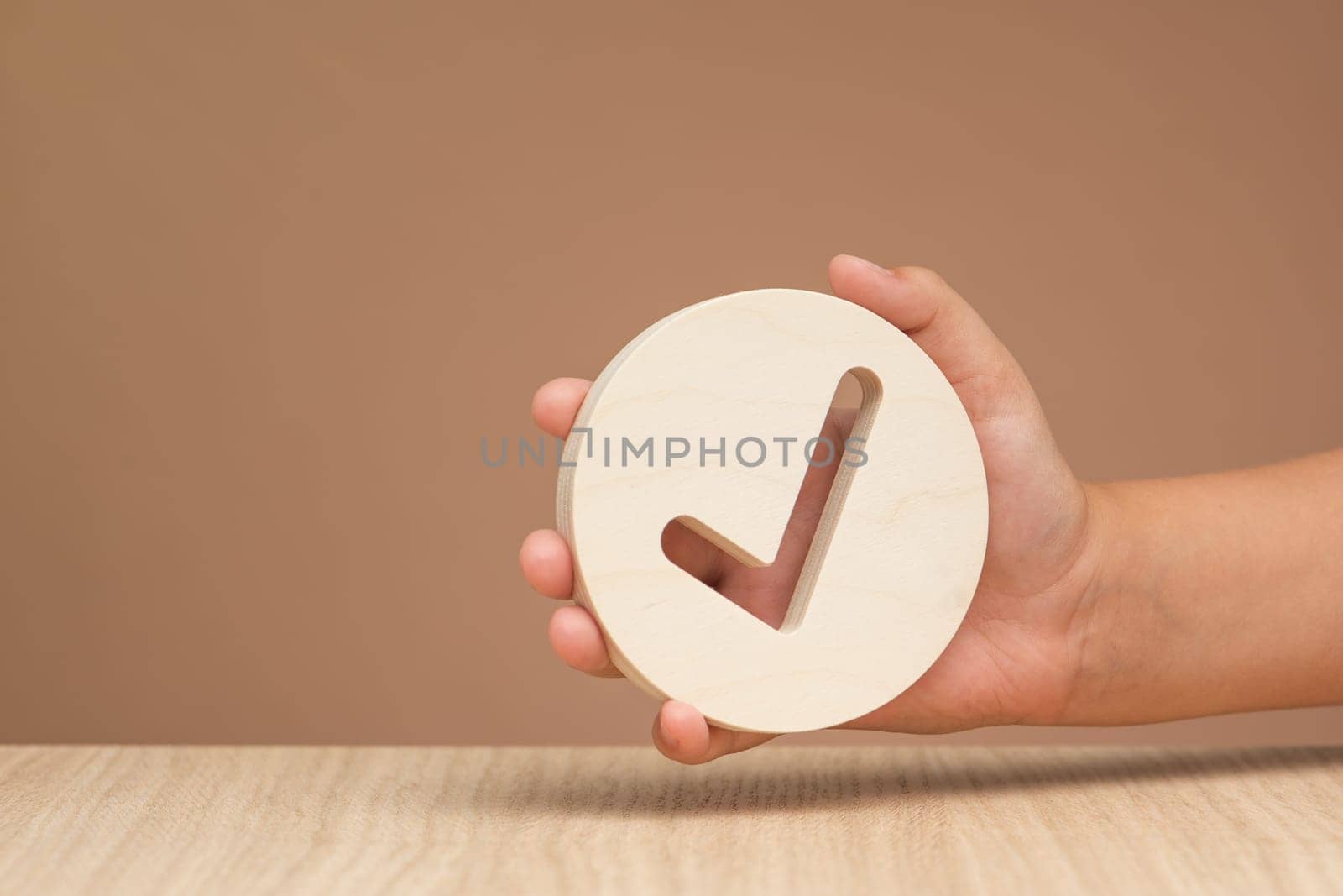 Hand holding check mark icon, banner with wooden check mark icon in hand, right sign. On a brown background. Copy space. Place for text. High quality photo