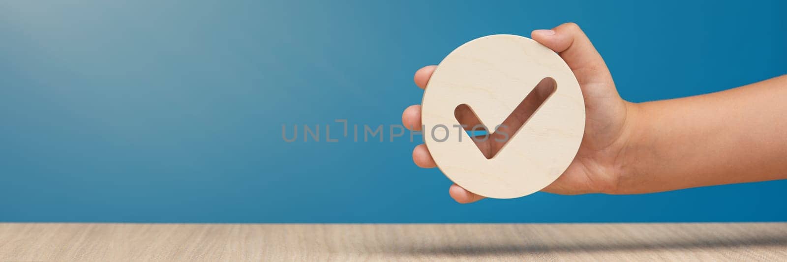 Hand holding check mark icon, banner with wooden check mark icon in hand, right sign. On a blue background. Copy space. Place for text by SERSOL