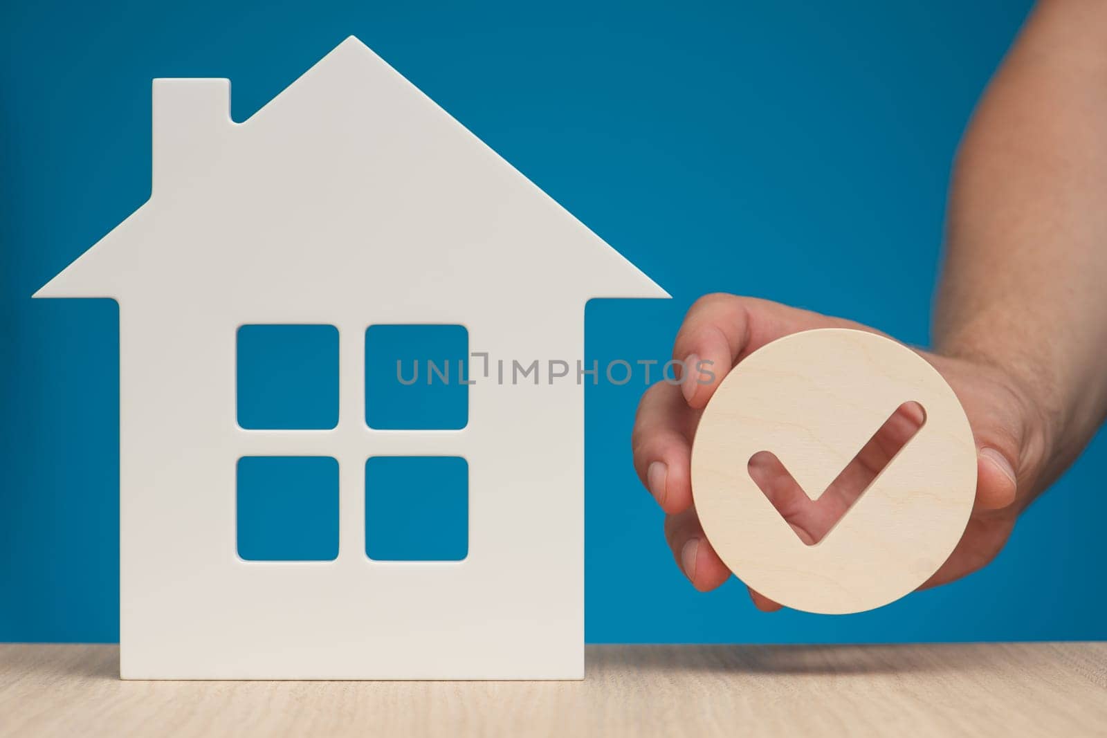 Real estate mortgage approval. Check mark icon in hand and house model as a symbol of a successful real estate purchase or sale deal. Photo with blue background and copy space