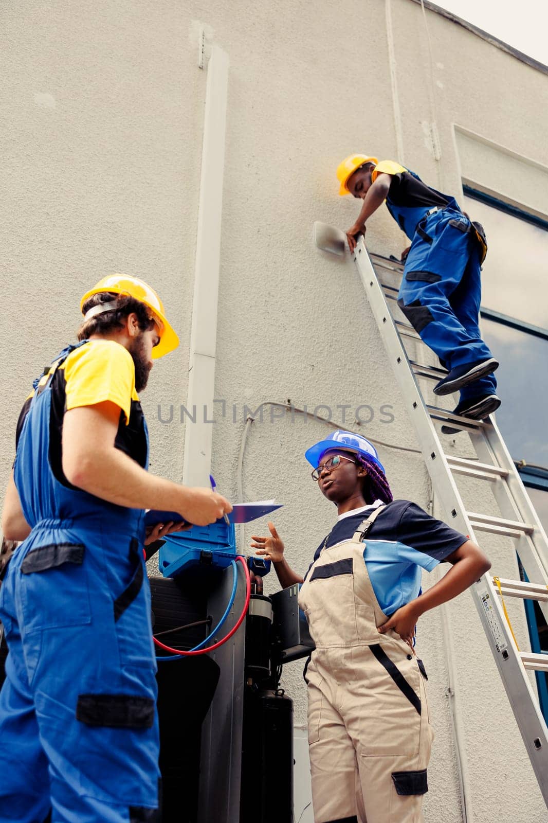Competent wiremen diverse coworkers commissioned for external air conditioner routine check up, writing findings on clipboard. Professionals doing hvac system investigation of damaged parts