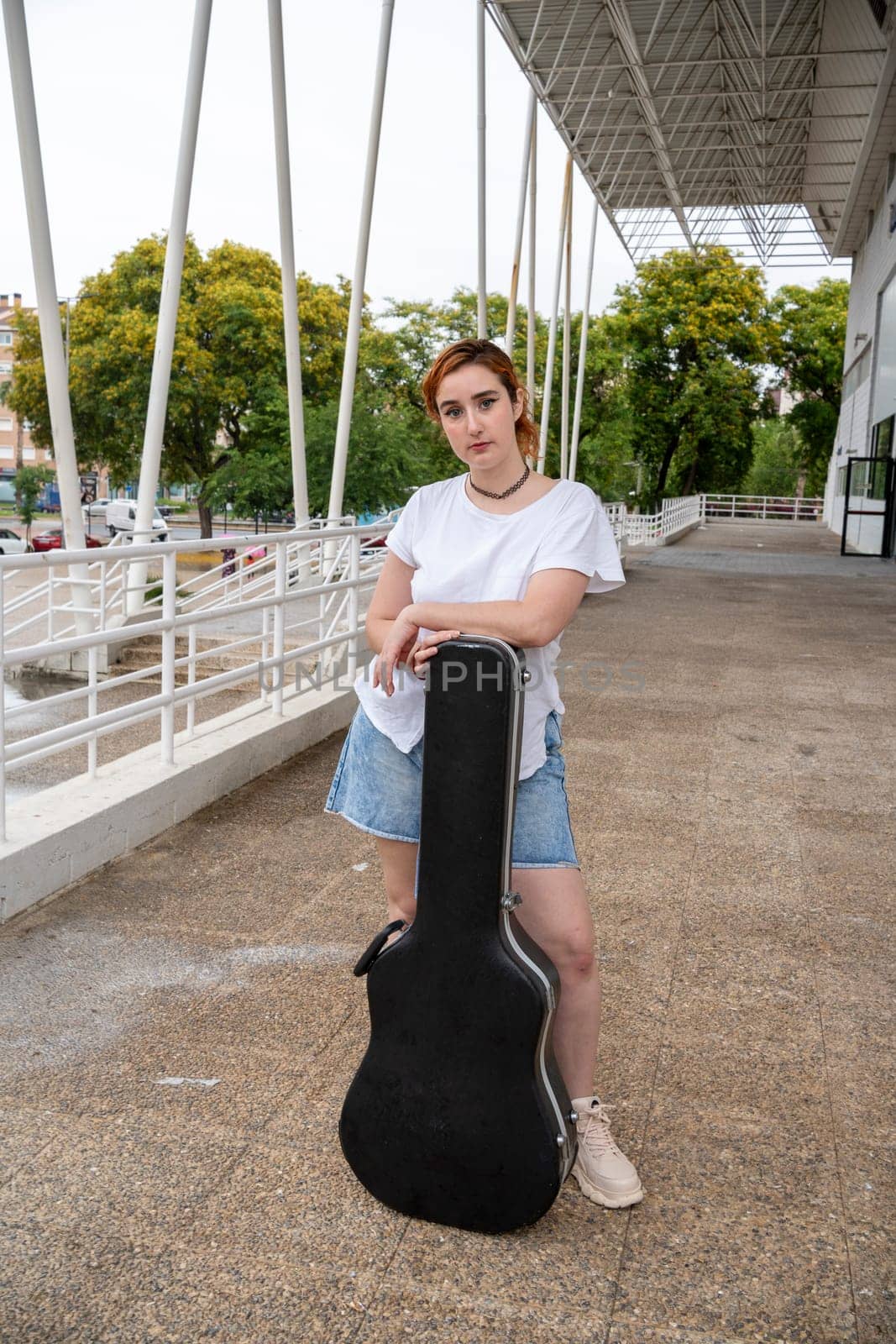 young woman from the front holding a guitar case, street music