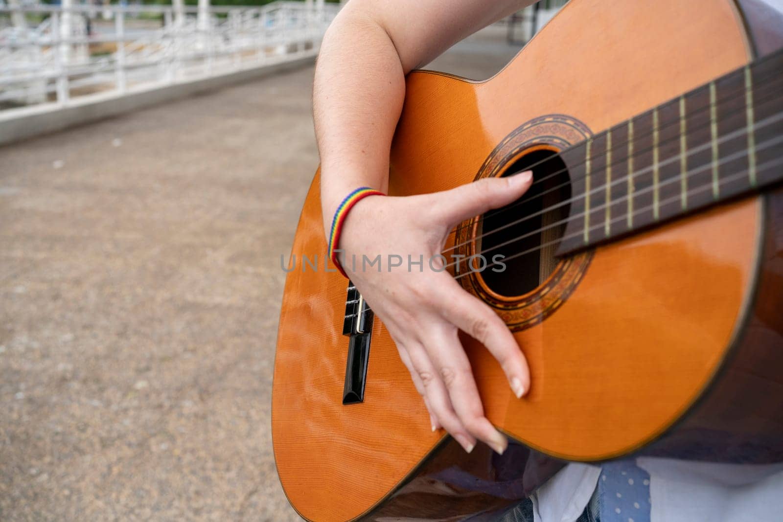 Crop anonymous female guitarist with LGBT wristband playing acoustic guitar while performing song on city street