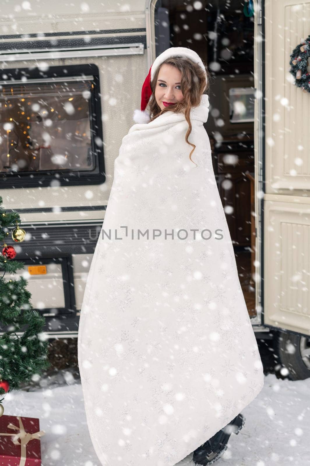 Young woman in santa costume decorates the Christmas tree at winter campsite getting ready for the new year. New year celebration concept