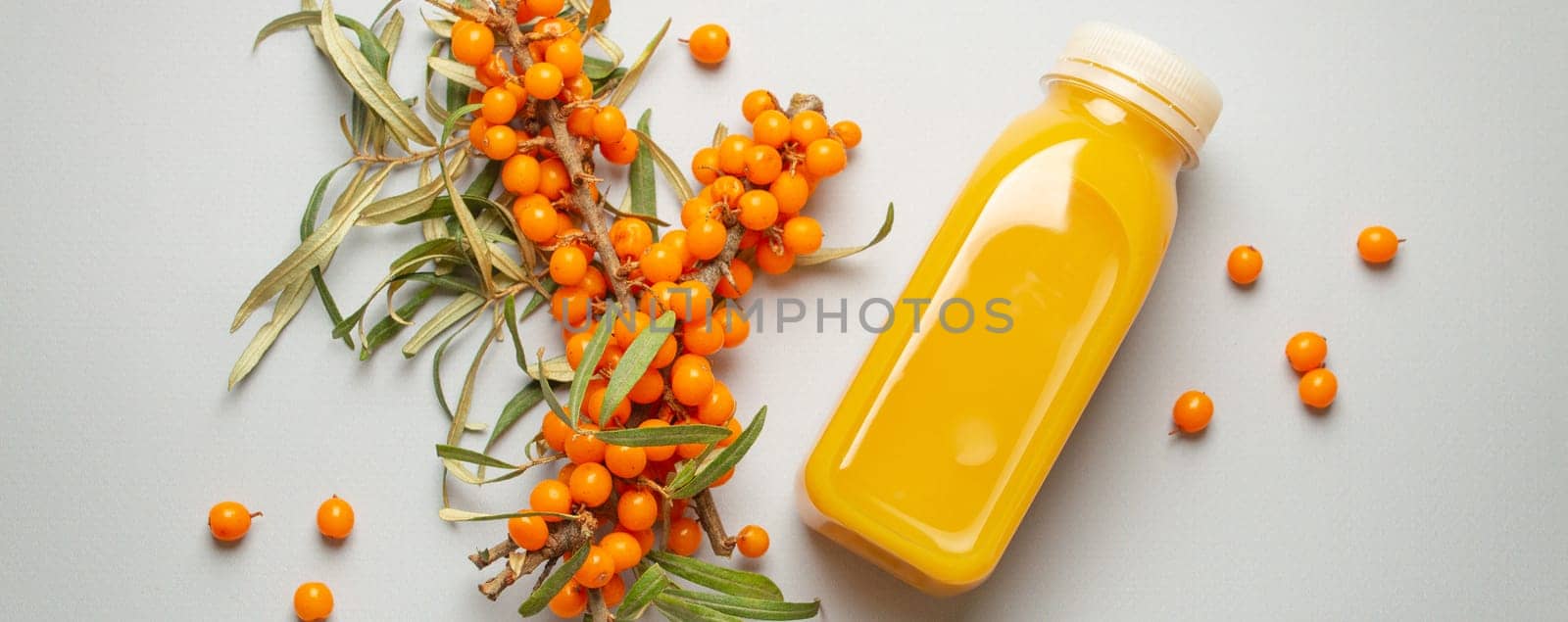 Sea buckthorn healthy juicy drink in bottle and branches with leaves and ripe berries top view on light grey simple background..