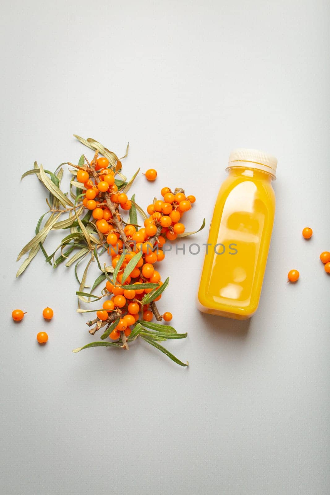 Sea buckthorn healthy juicy drink in bottle and branches with leaves and ripe berries top view on light grey simple background. by its_al_dente