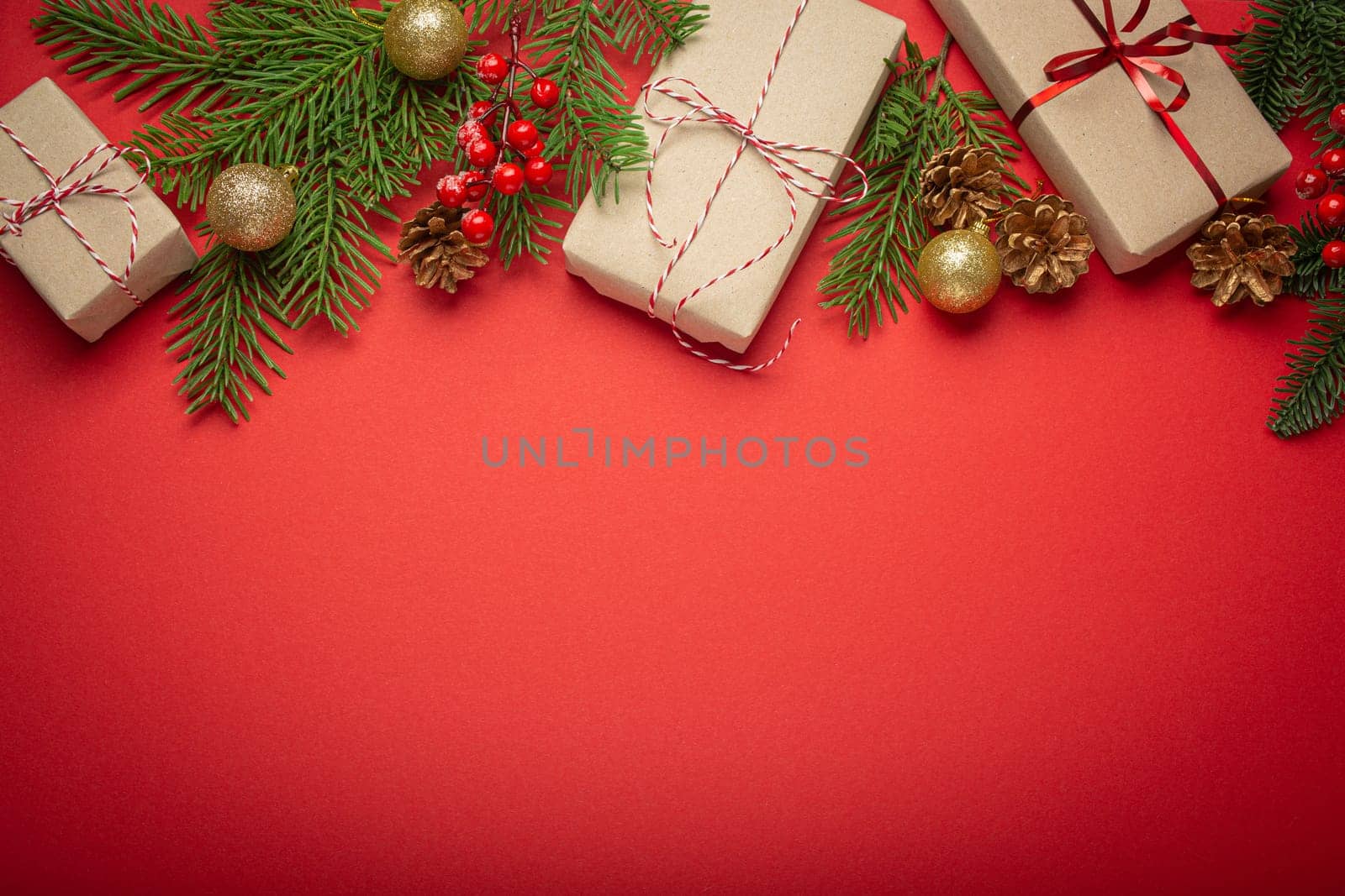 Christmas or New Year celebration red paper festive background with decoration fir tree, wrapped present boxes, cones, berries, sparkly red balls. Space for text..
