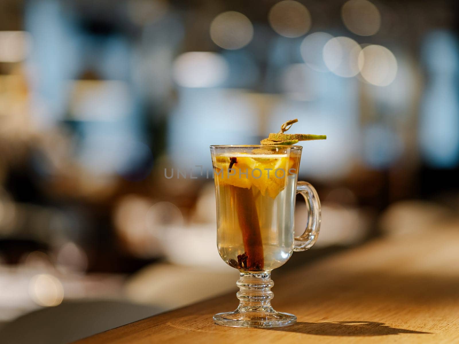 Glass with hot natural mulled cider drink made with cinnamon stick, mango and spices, on bar counter in restaurant interior. Warming beverage for cold season. Autumn or Christmas seasonal drink