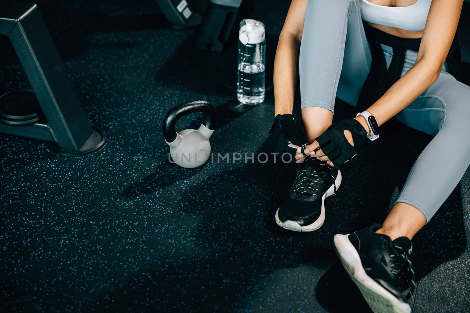 Close-up of a young woman tying her shoelaces before hitting the gym. The shot captures her slim legs and stylish sneakers. Fitness and fashion concept.