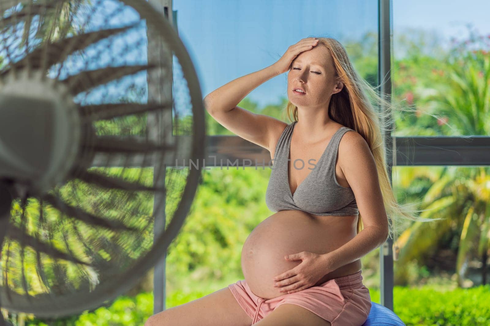 A pregnant woman seeks relief from an abnormal heatwave by using a fan, ensuring her comfort and well-being during sweltering conditions by galitskaya