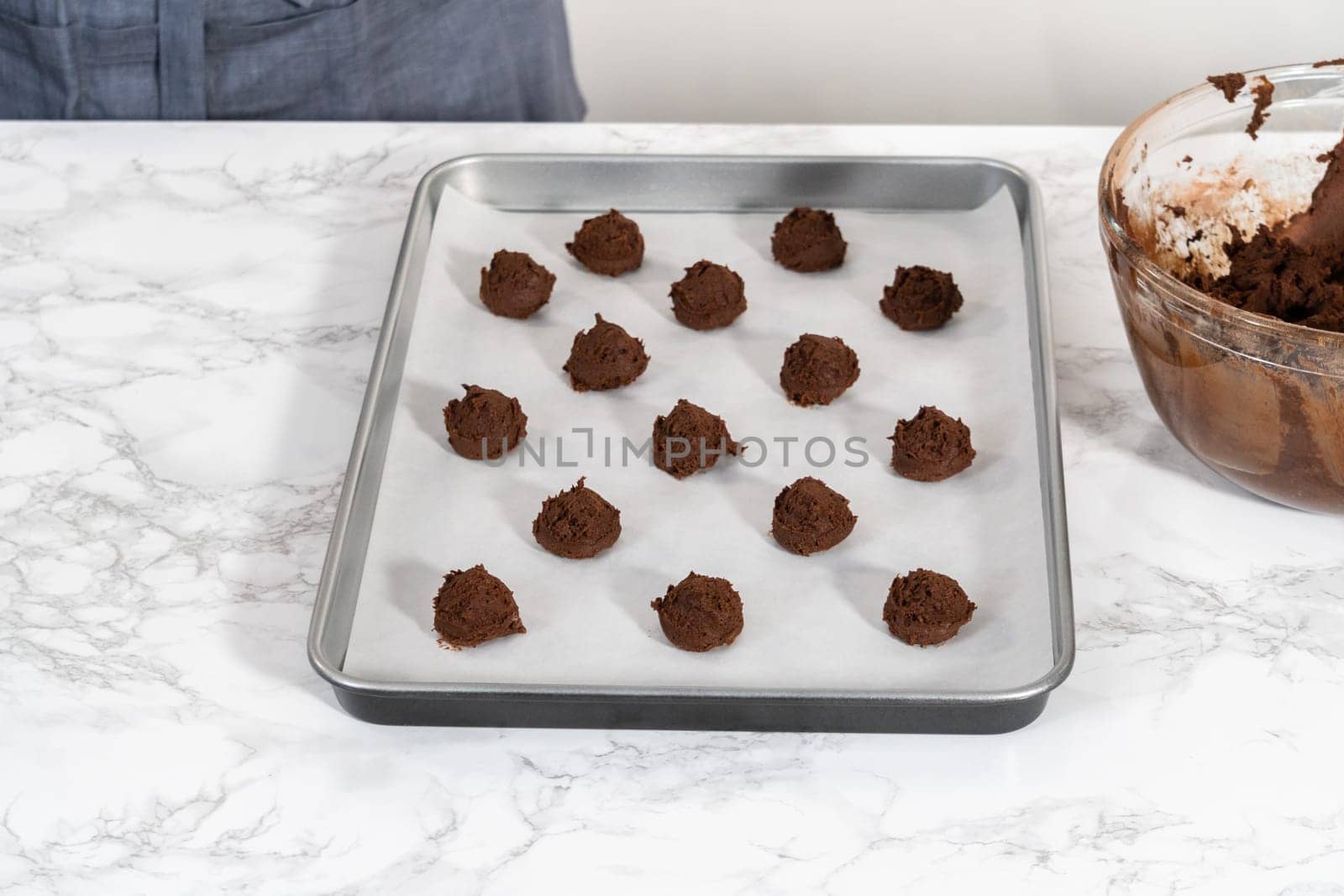 Scooping cookie dough with dough scoop into a baking sheet lined with parchment paper to bake chocolate cookies with chocolate hearts for Valentine's Day.