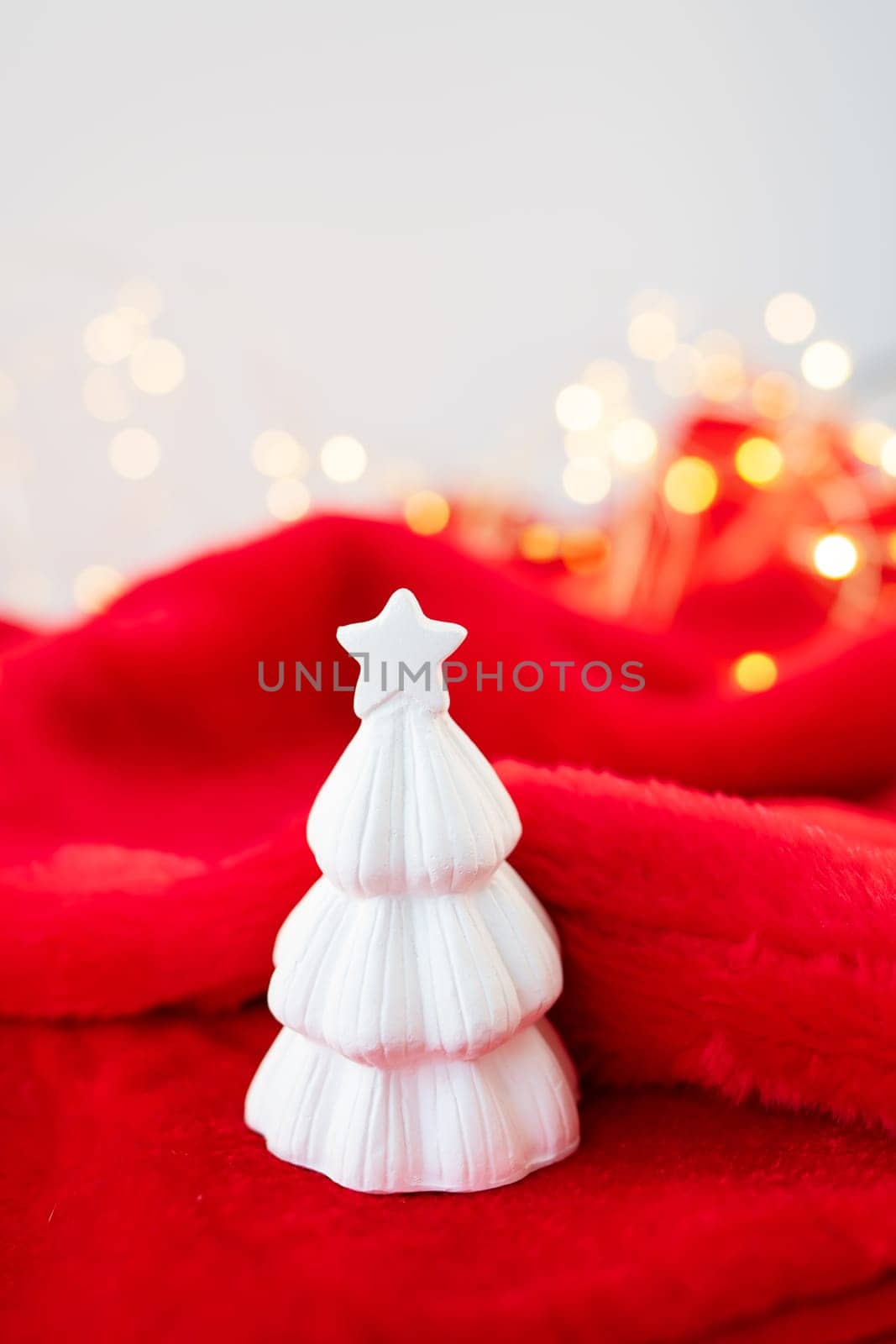 Christmas home interior with a white ceramic Christmas tree on a red blanket. Christmas and New Year concept. Vertical photo