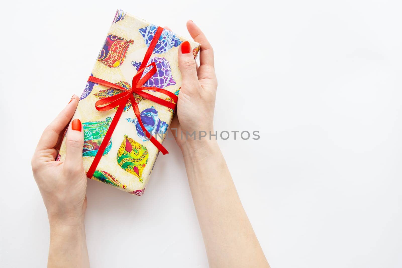 The girl holds a gift in her hands with a red ribbon and multi-colored paper on a white background. Time to wrap presents. Surprise, Christmas and New Year concept