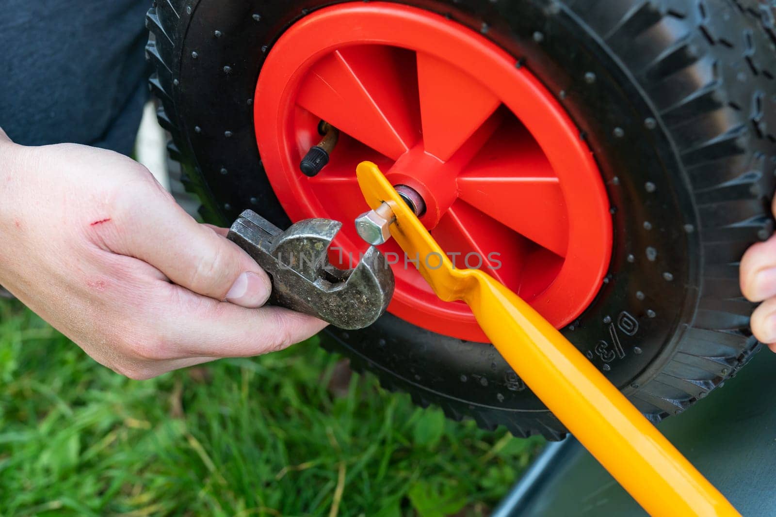 A man repairs a garden wheelbarrow, unscrews the bolts, fastens the wheel. Farm work, seasonal cleaning before autumn. On the street
