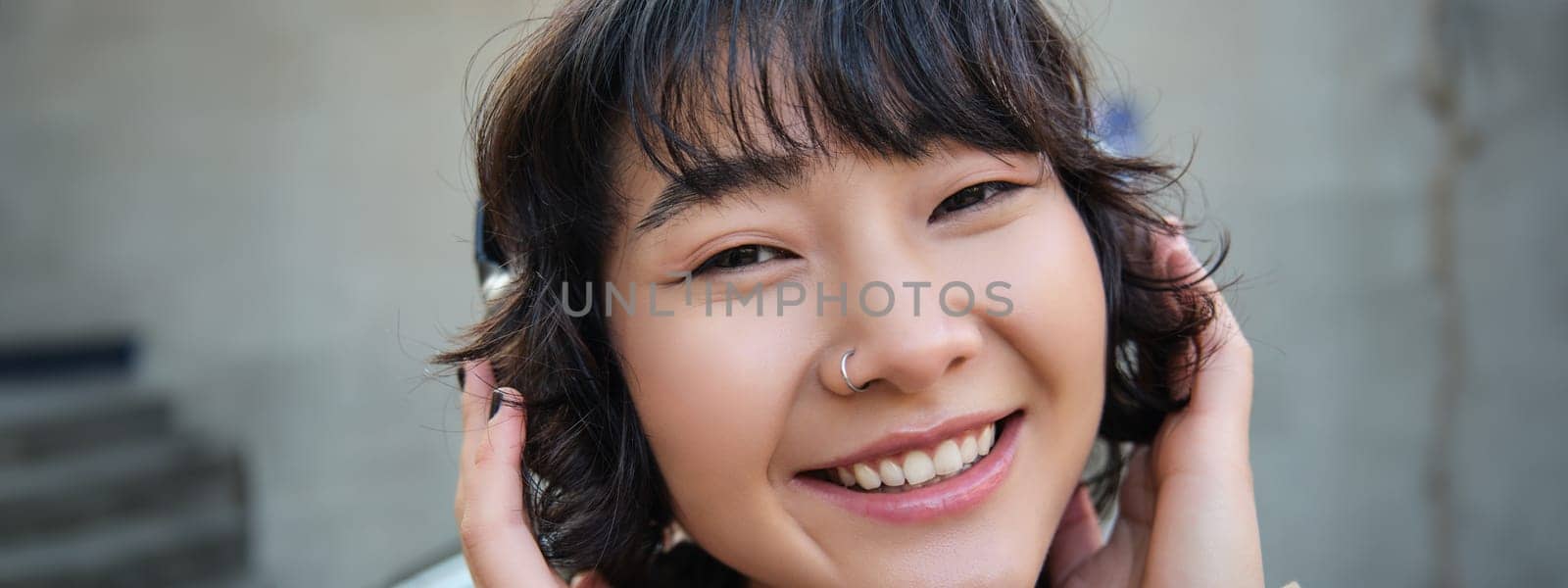 Portrait of happy woman, korean girl in headphones, listening music in headphones, enjoying sound of earphones, laughing and smiling.