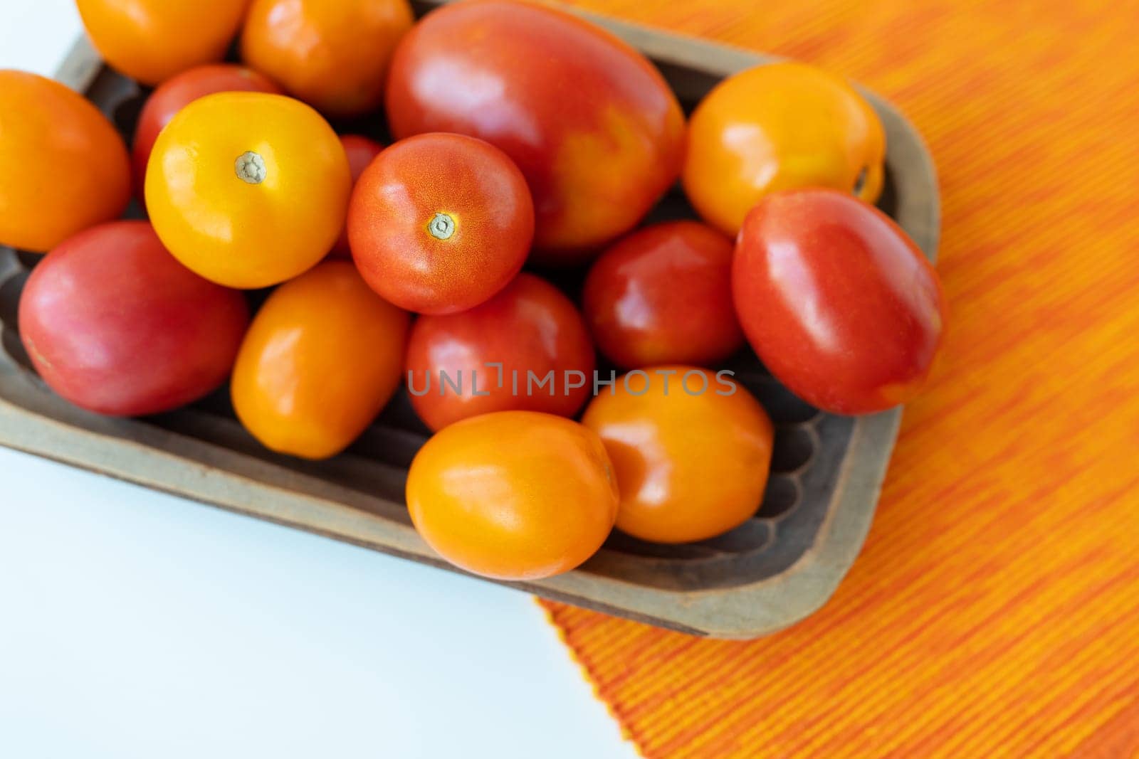 Fresh bright multi-colored red-yellow tomatoes in a wooden plate on the table. View from above