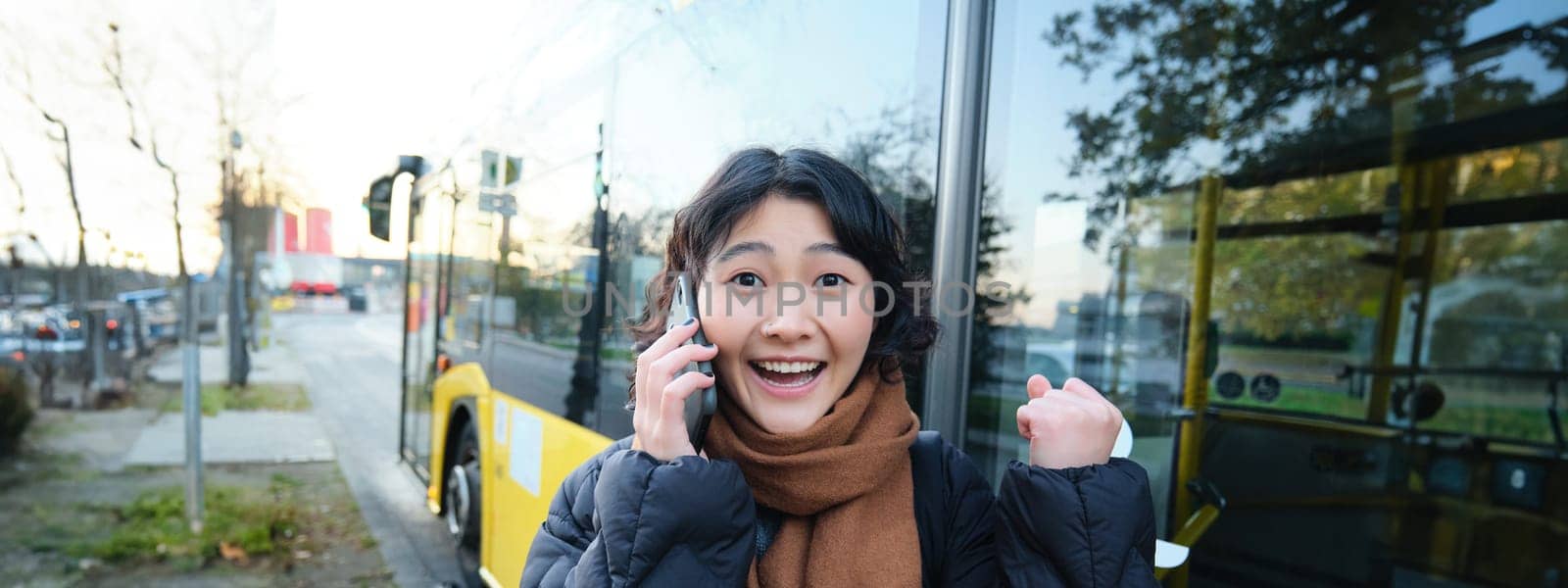 Happy asian girl talks on mobile phone and looks surprised, amazed by great news, achieve goal, hear something exciting by Benzoix