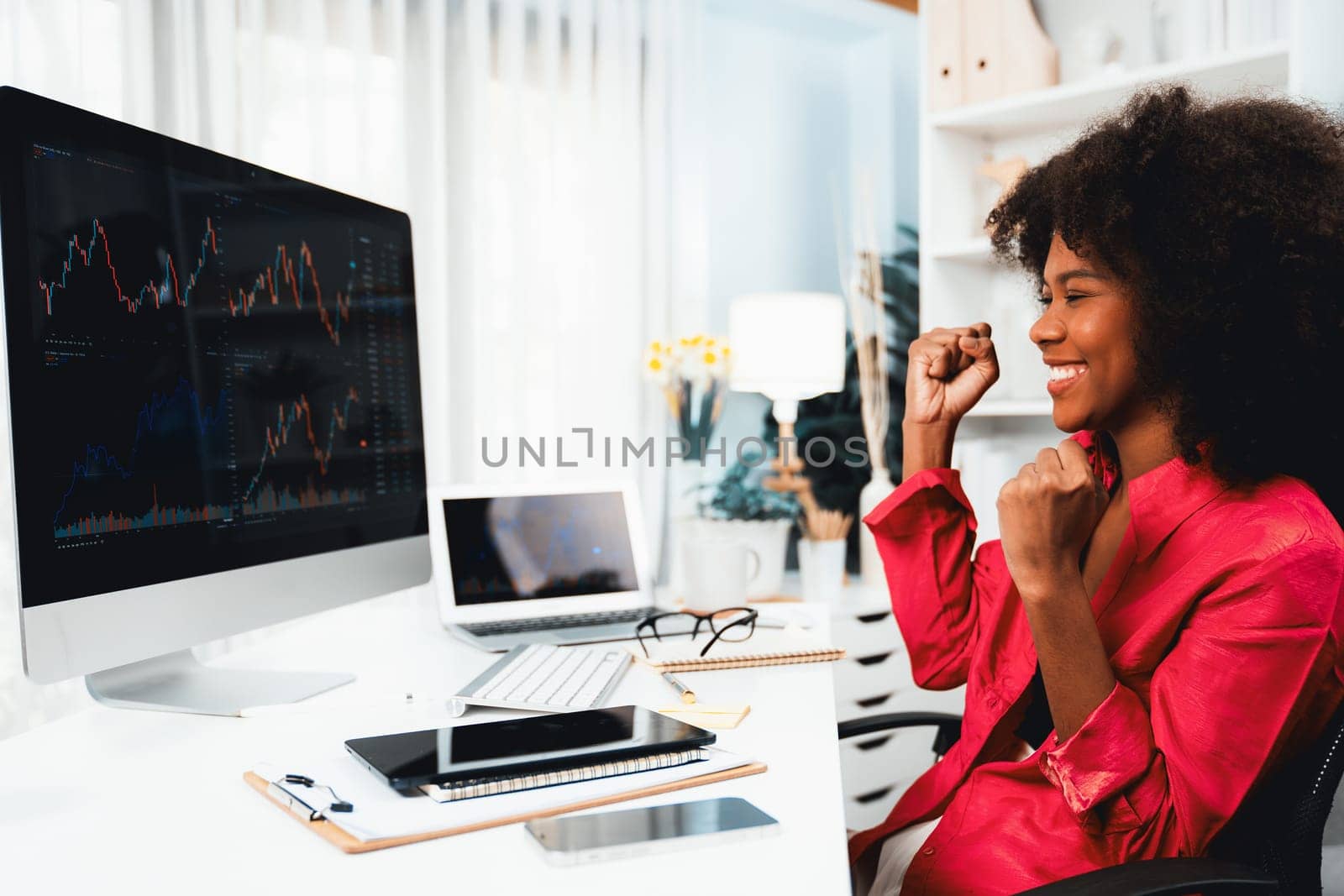 African woman blogger smiling on happy face, looking on screen with valued stock market achievement at high profit. Concept of exchange investment online in trading application on pc. Tastemaker.