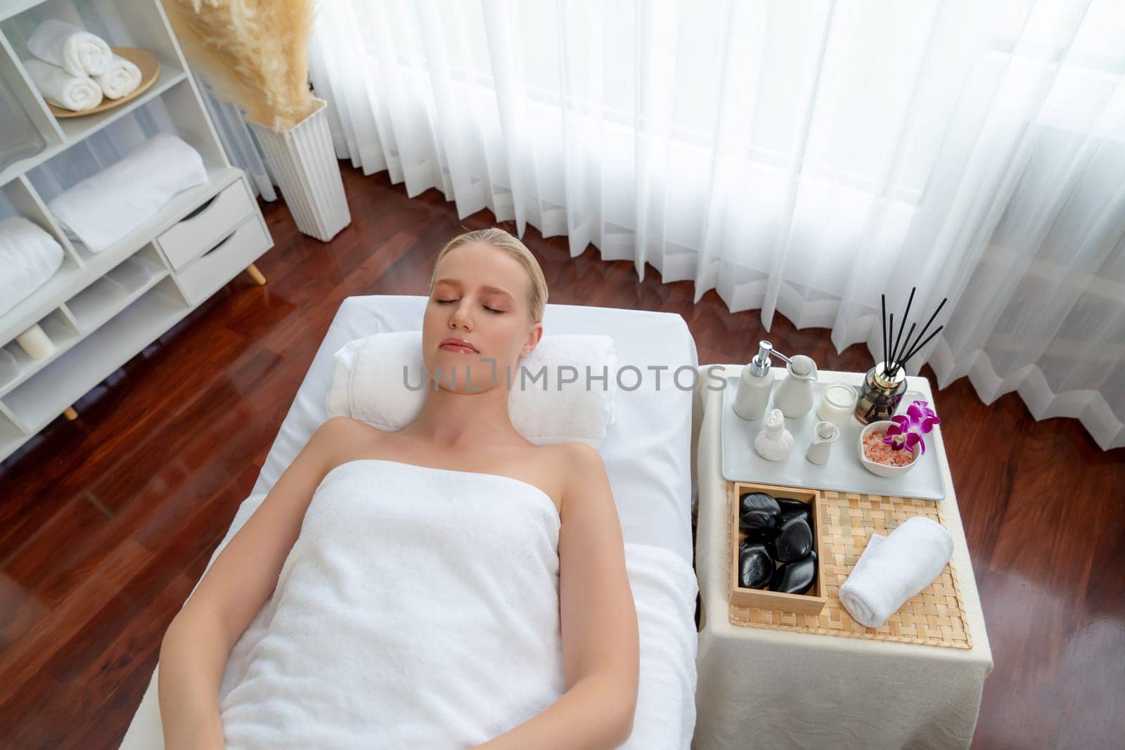 Caucasian woman customer enjoying relaxing anti-stress spa massage and pampering with beauty skin recreation leisure in day light ambient salon spa at luxury resort or hotel. Quiescent