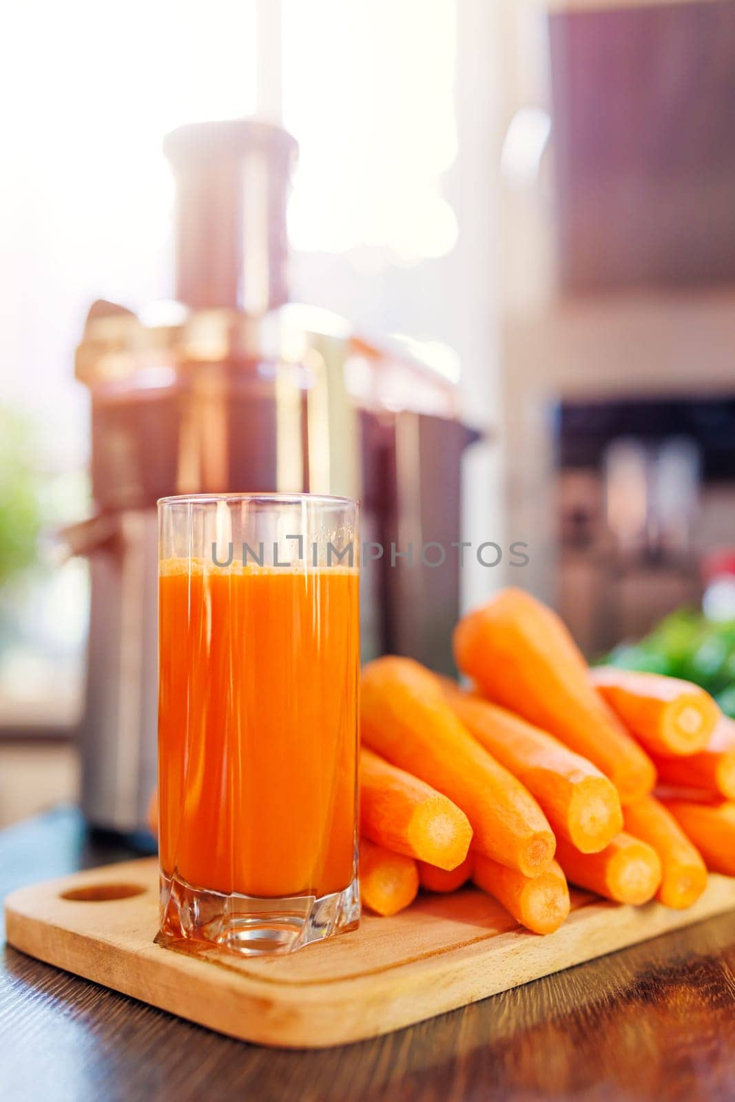 Glass of freshly squeezed carrot juice, carrots and juicer in the kitchen. Healthy lifestyle concept