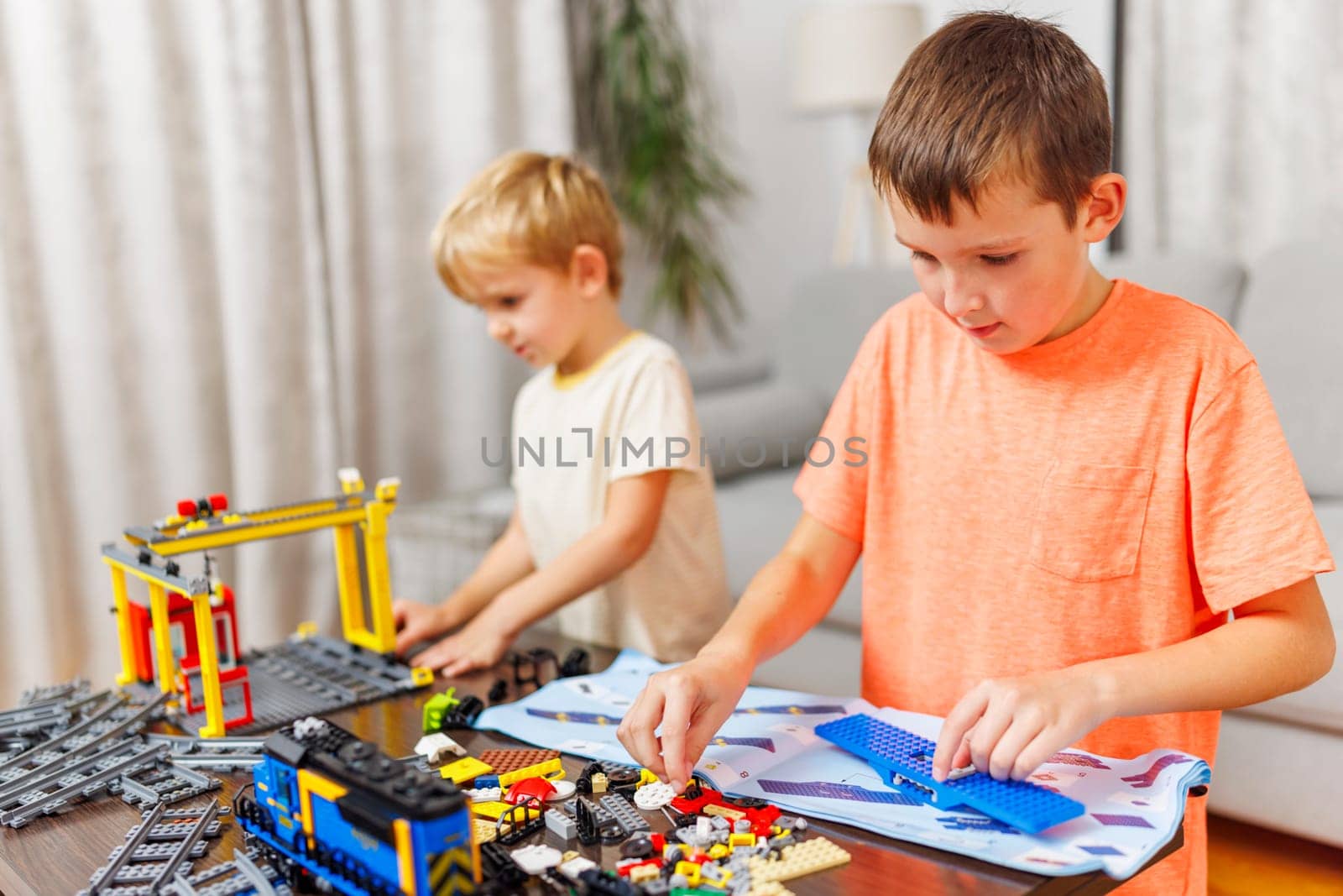 Two children playing and building with colorful plastic bricks at the table by andreyz
