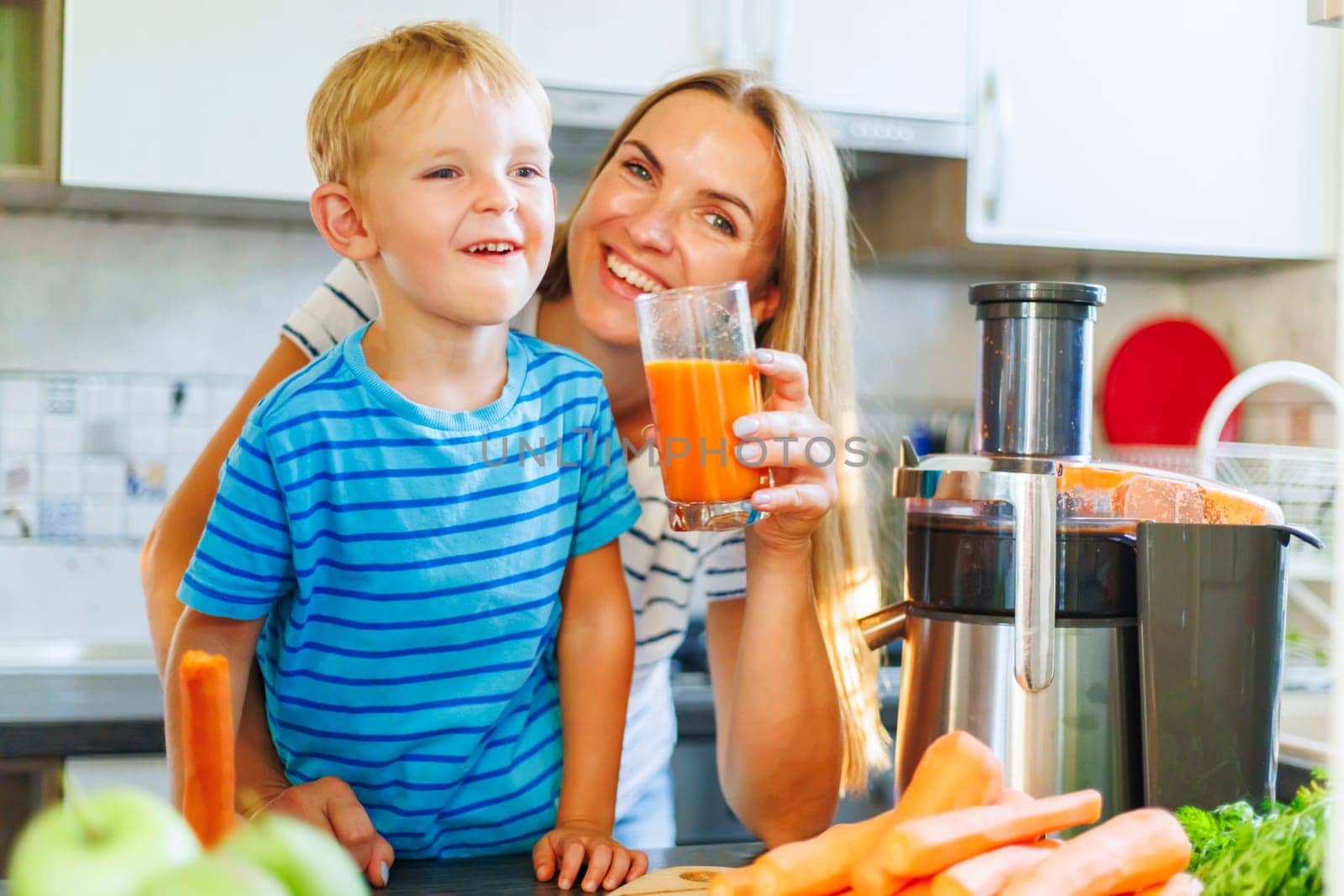 Mom and son drink fresh carrot juice squeezed using juicer in kitchen at home by andreyz