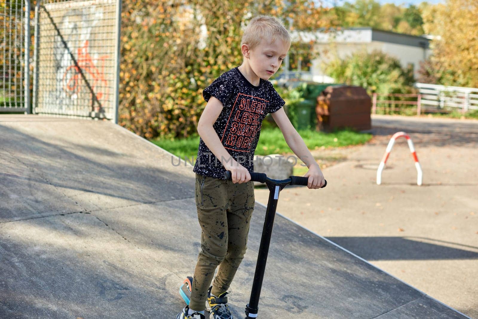 Child on kick scooter in park. Kids learn to skate roller board. Little boy skating on sunny summer day. Outdoor activity for children on safe residential street. Active sport for preschool kid. boy kid Roller park by Andrii_Ko