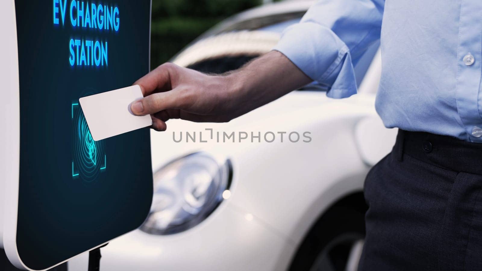 Businessman pay electric vehicle's eco-friendly and sustainable energy scanning credit card at charging station. Payment to power up his rechargeable electric vehicle at charging point. Peruse