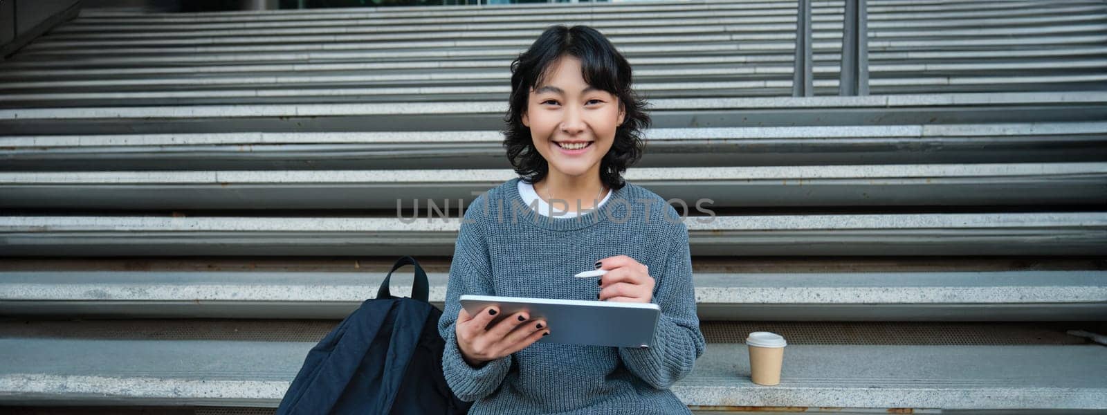 Portrait of asian girl student, hipster sitting on stairs with digital tablet and cup of coffee, draws digital art, makes design project by Benzoix