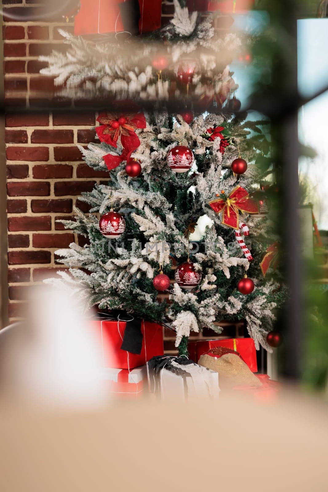 Artificial christmas tree decorated with red baubles behind window in brick wall office. Festive evergreen with ornaments during new year winter holiday season in corporate workplace