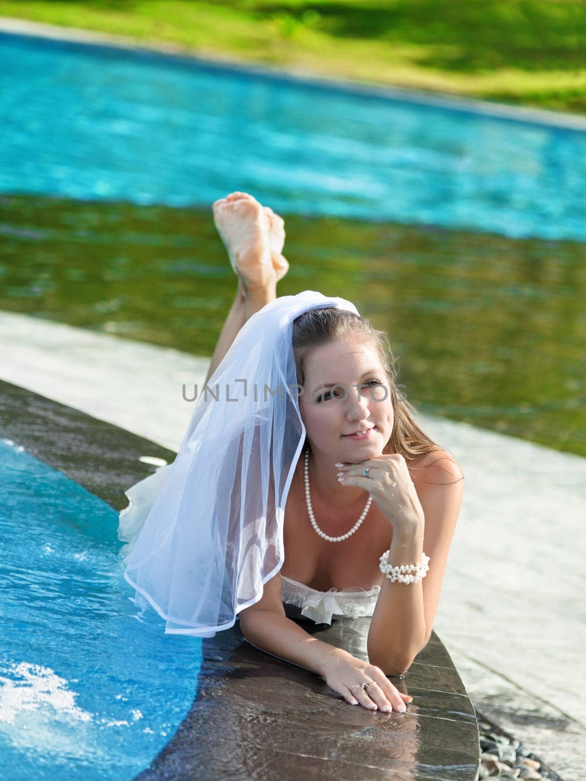 Funny bride lies on the edge of swimming pool