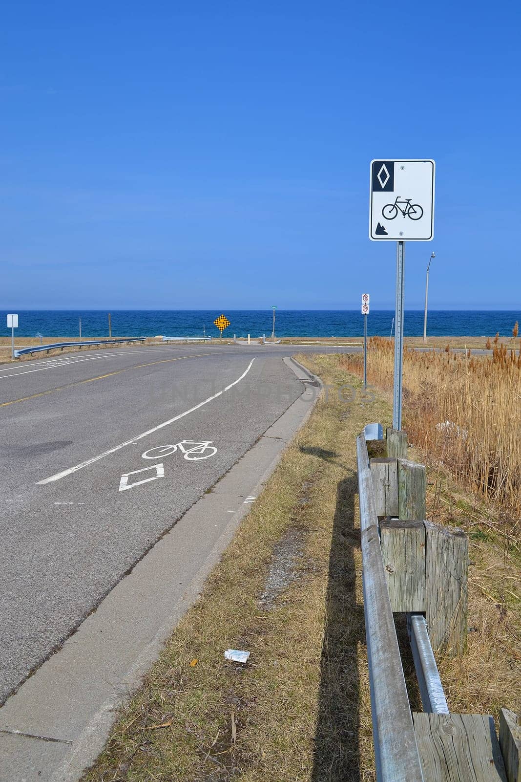 On a rural road in Stoney Creek, Ontario, a sign and markings on the street shows this is a designated lain for bicycles, background lake Ontario.